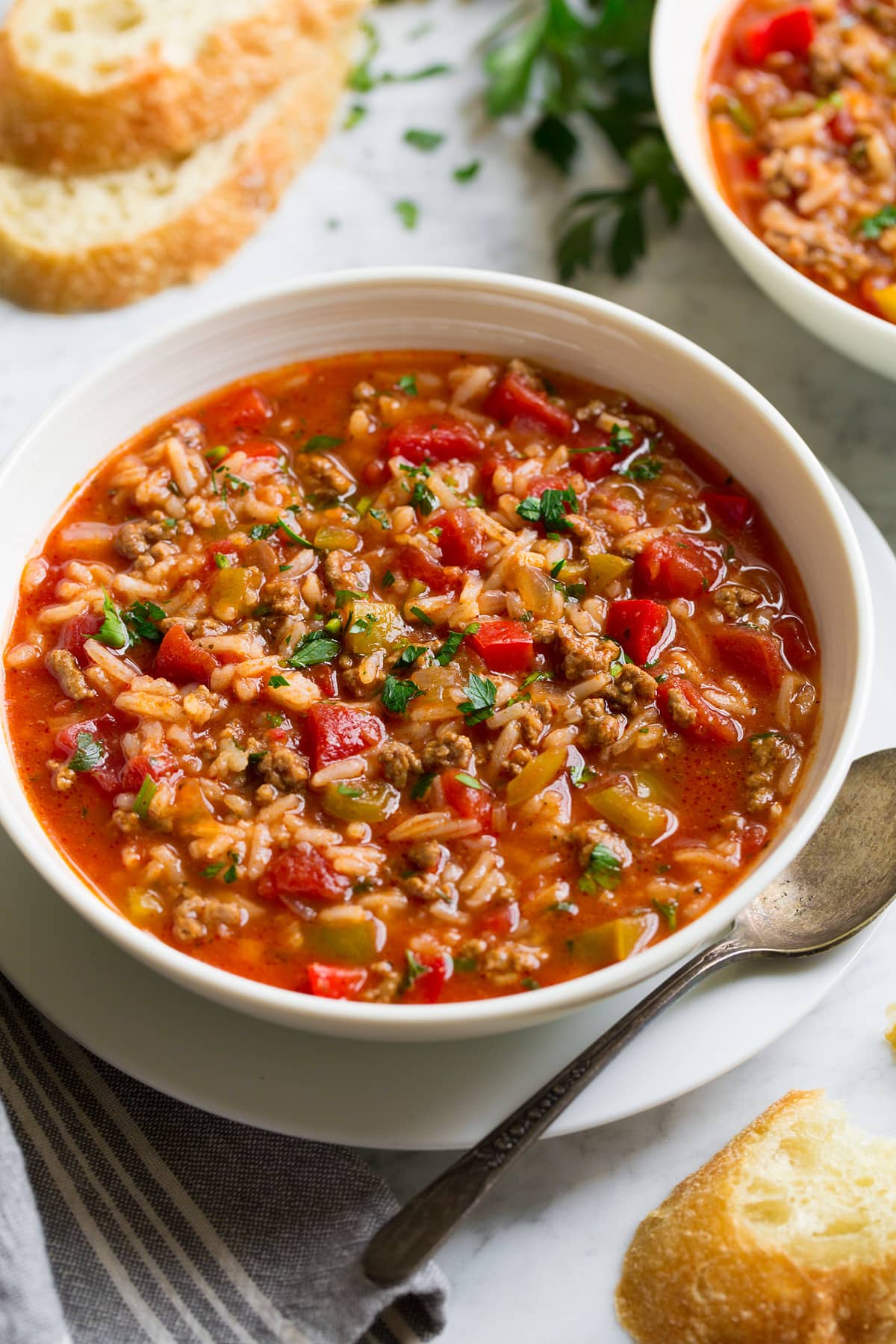 Single Serving of Stuffed Pepper Soup in a white serving bowl set over a white plate with a spoon and bread to the side.