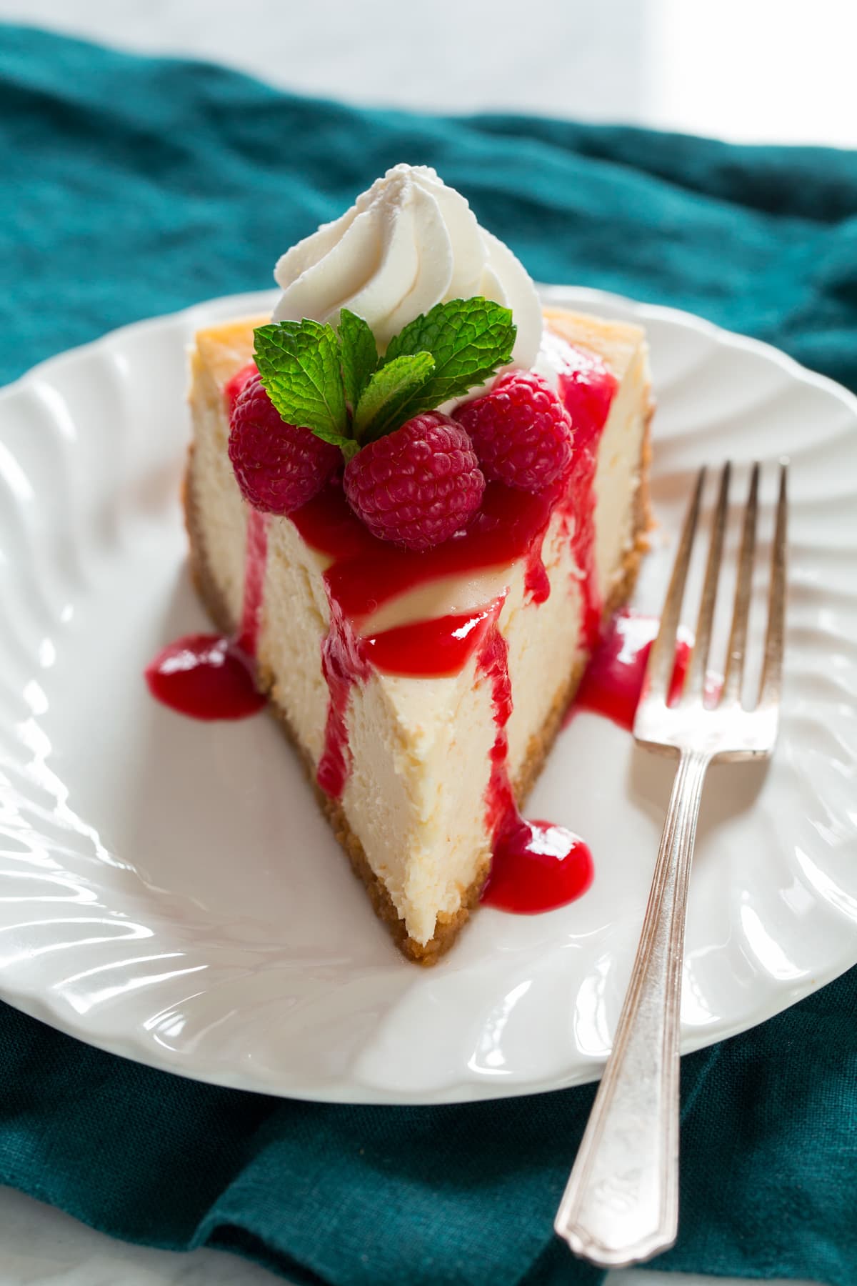 Slice of cheesecake topped with raspberry sauce, fresh raspberries, whipped cream and mint.