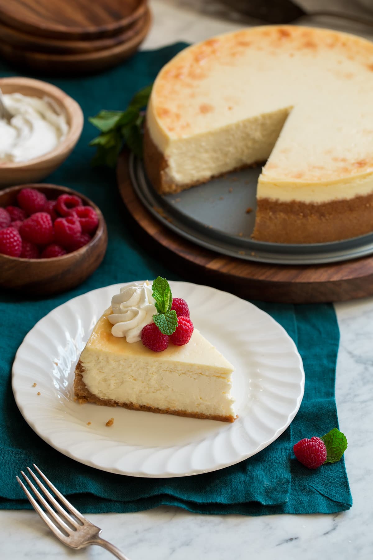 One slice of cheesecake with whole cheesecake in background.