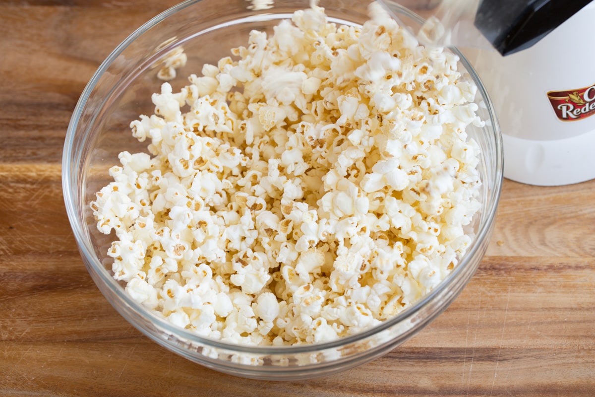 Popping popcorn into a glass bowl using an electric popcorn machine.