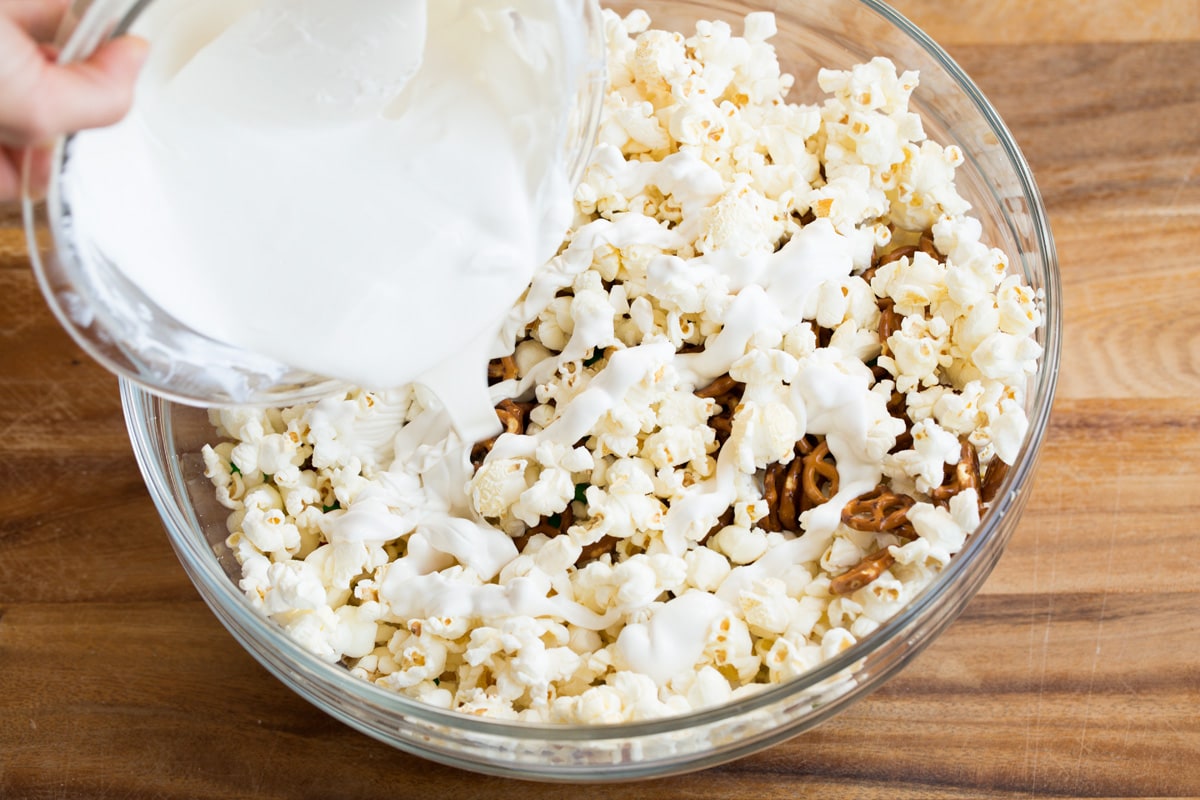 Pouring melted white chocolate candy coating over popcorn.