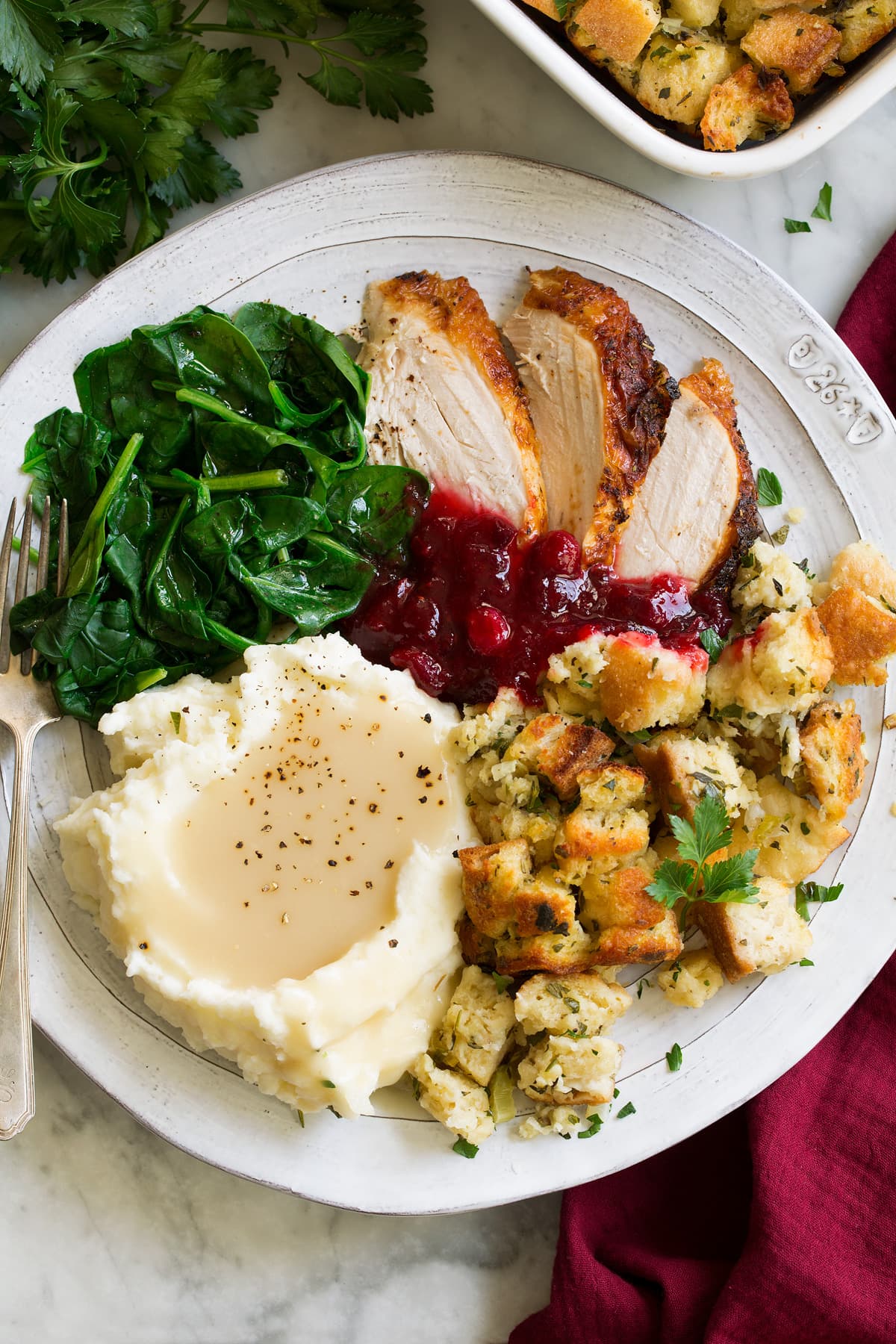 Stuffing on a large dinner plate with a side of mashed potatoes and gravy, turkey and steamed spinach.