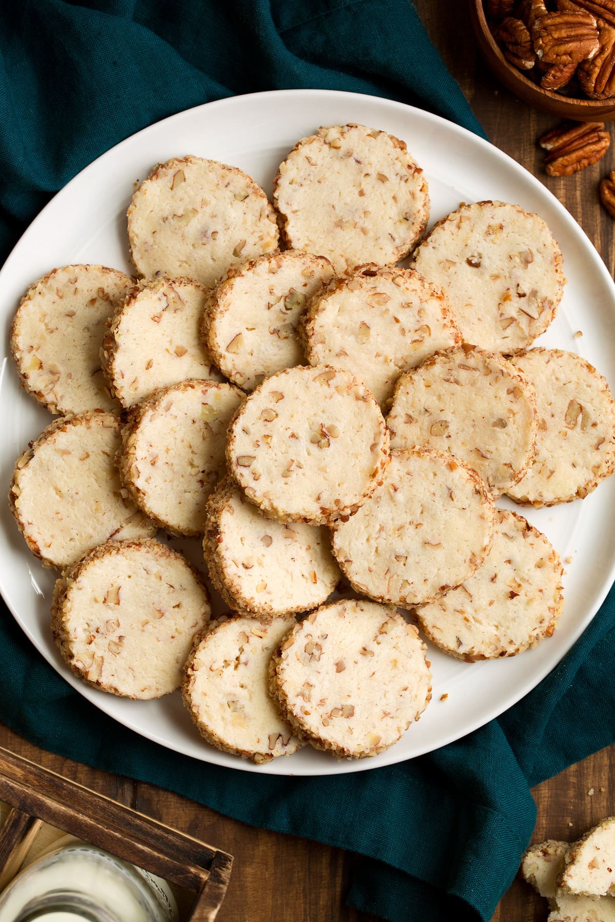 Overhead image of cream cheese pecan cookies stacked on a white serving plate set over a blue cloth.