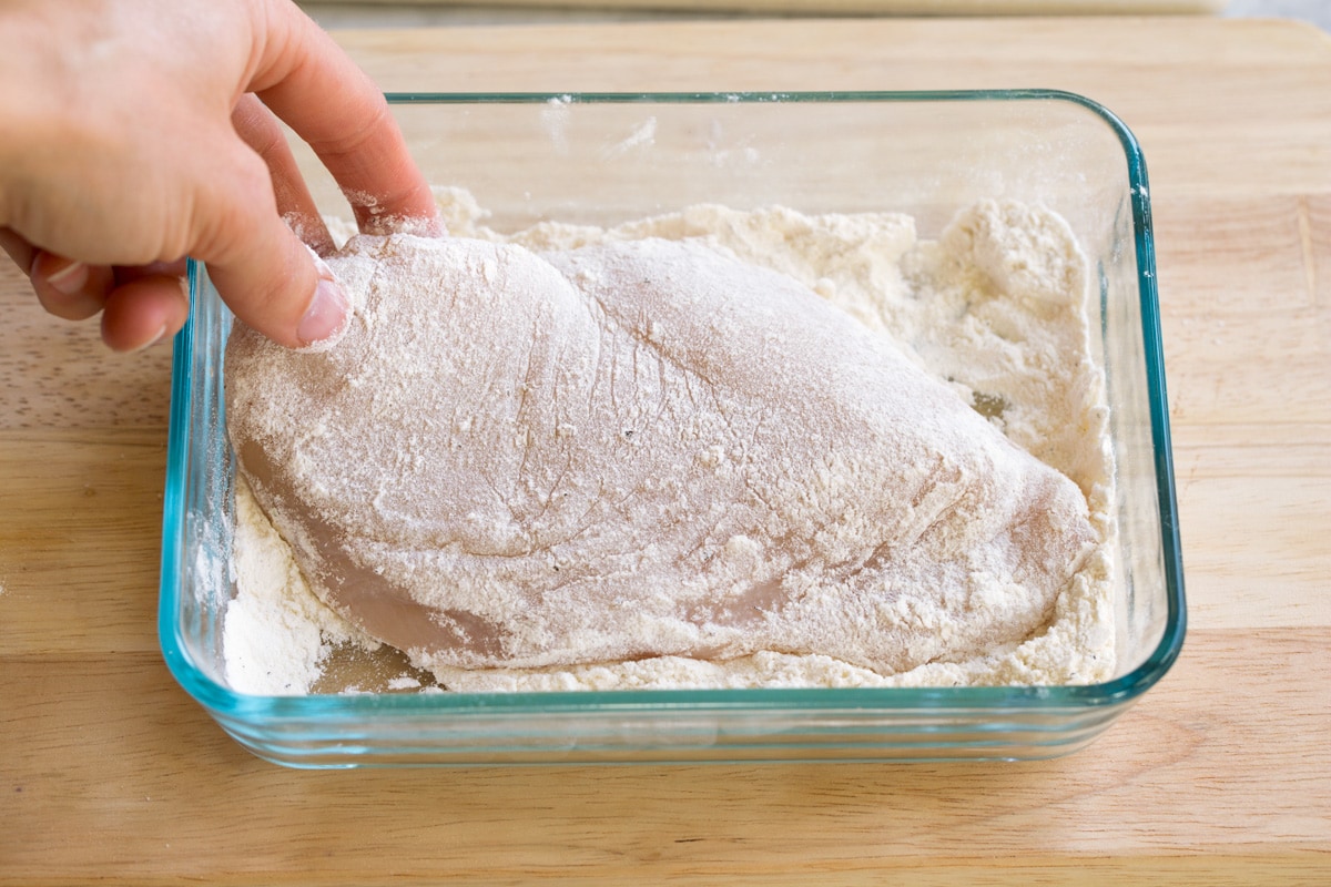 Dredging pounded chicken breasts in flour in a shallow dish.