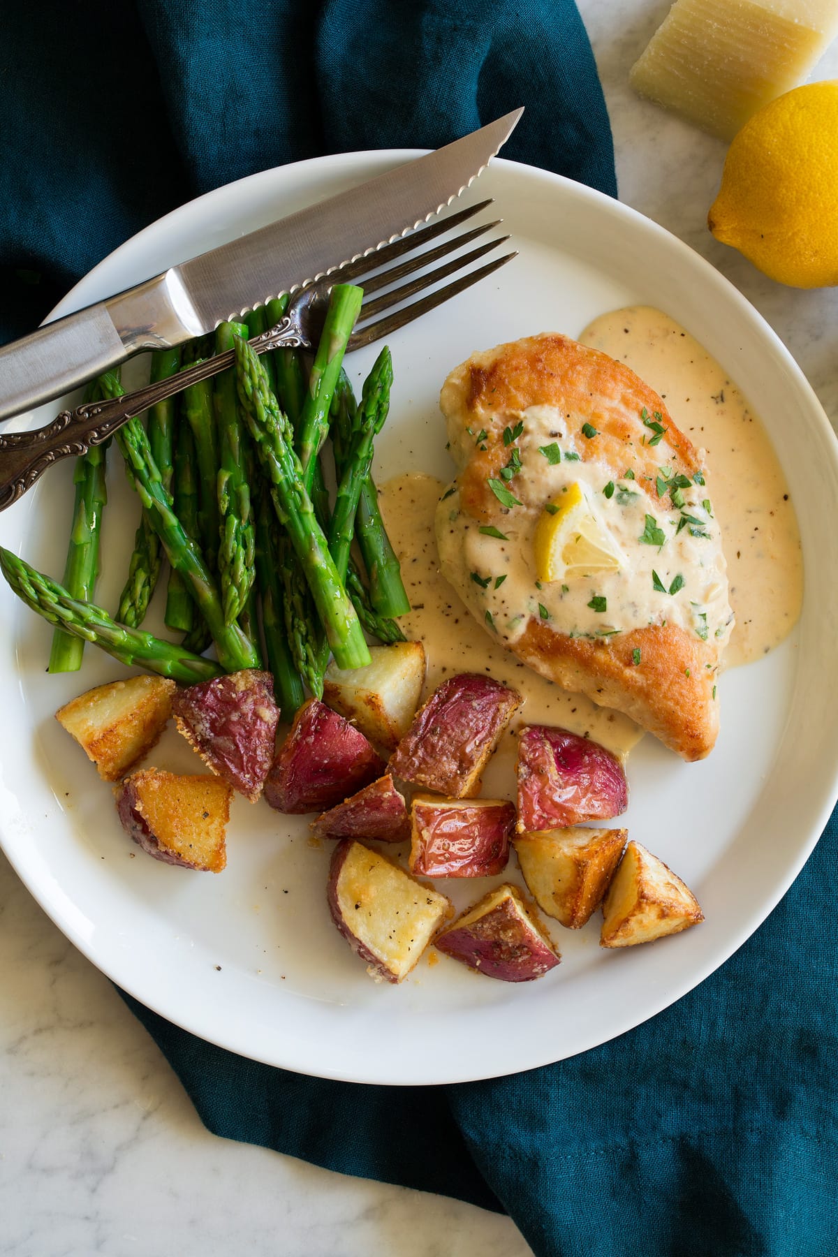 Plate with chicken breast topped with creamy lemon romano sauce and sides of potatoes and asparagus. 