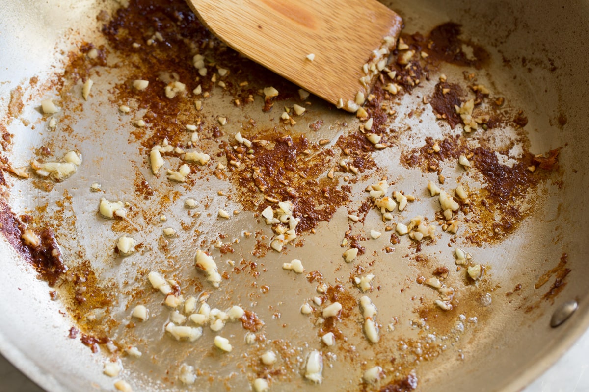 Stainless steel skillet with sauteed garlic and browned bits on bottom.