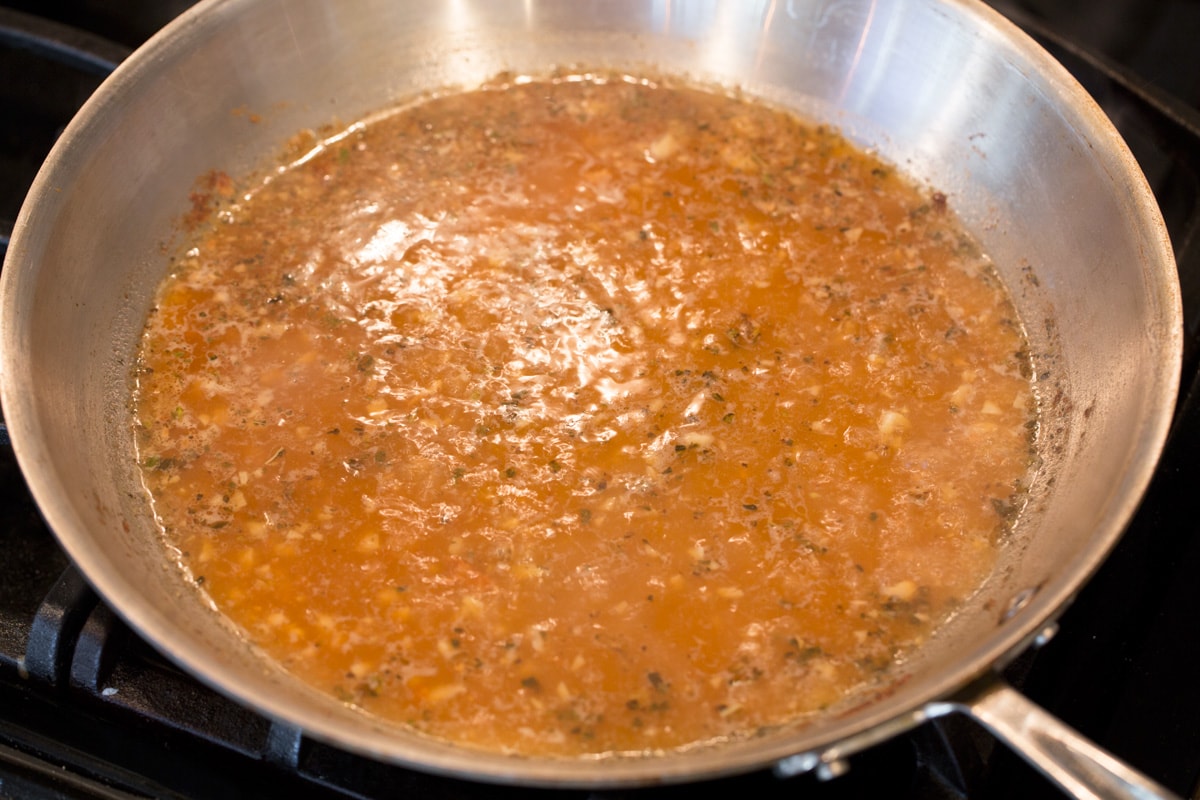 Simmering and reducing sauce in the stove top in a large pan.