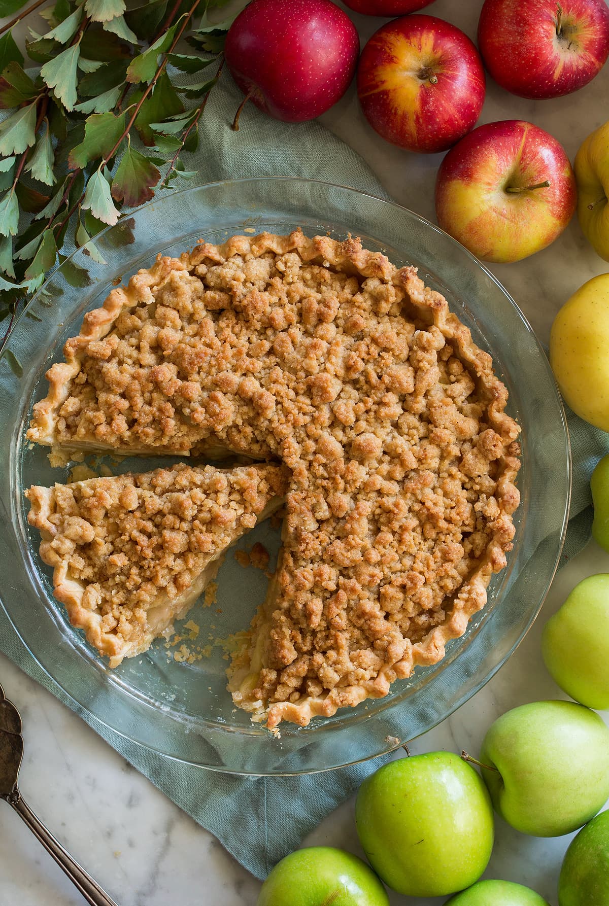 Overhead image of sliced Dutch apple pie with a colorful variety of apples around the pie.