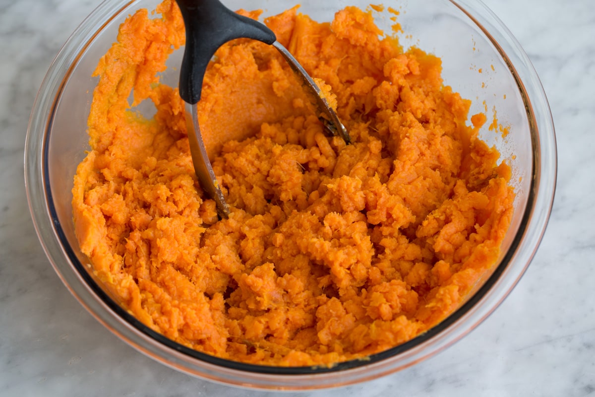 Mashed Sweet Potatoes - one of the best fall side dishes! These really are the best mashed sweet potatoes the secret ingredient is the browned butter! #mashedpotatoes #sweetpotatoes #sidedish #thanksigving Mashing sweet potatoes in a glass mixing bowl with a potato masher.