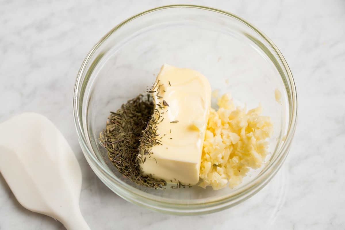 Making butter garlic herb mixture in a glass mixing bowl.