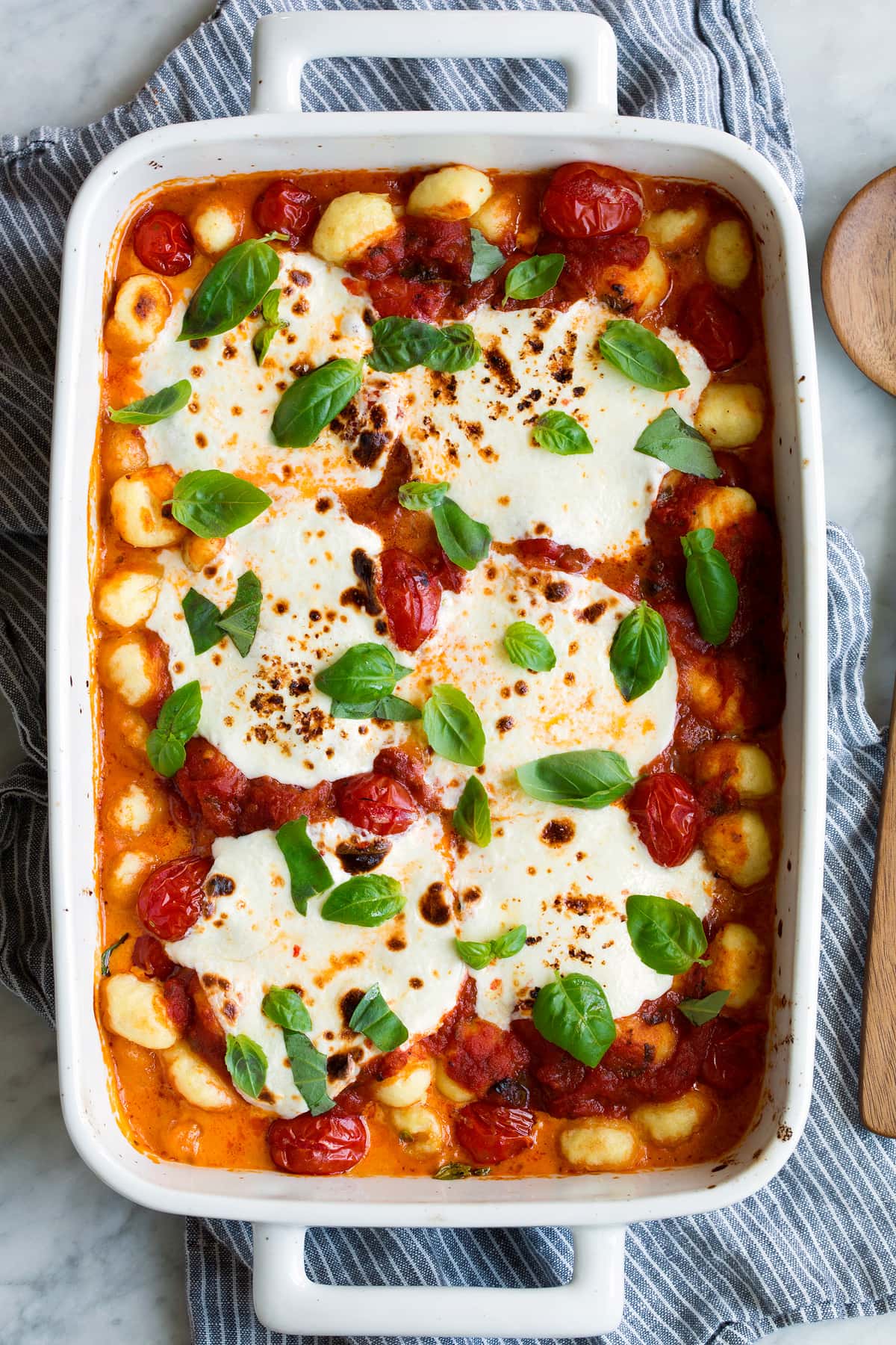 Baked Gnocchi in a white baking dish with marinara sauce, mozzarella and basil. 
