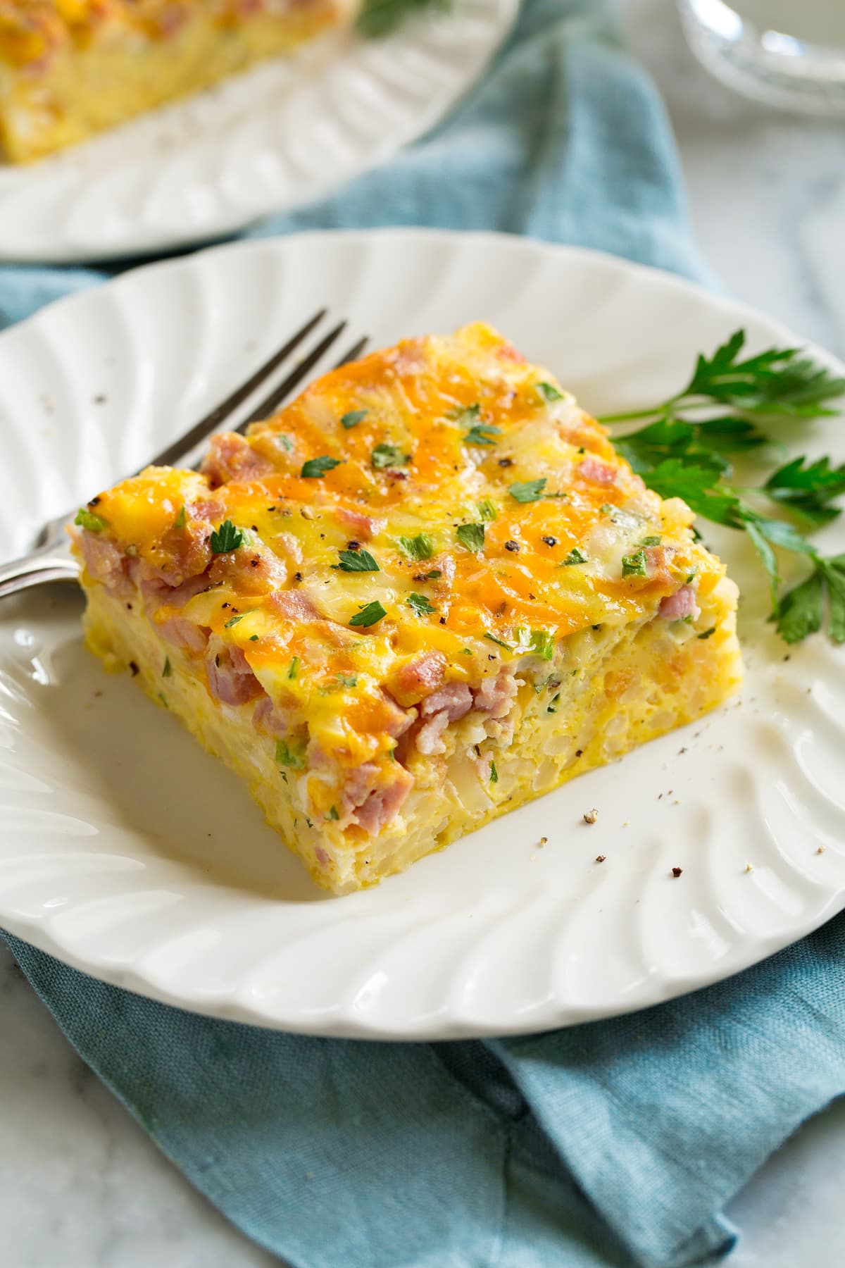 Slice of breakfast casserole filled with eggs, hash browns, ham and cheese on a white serving plate.