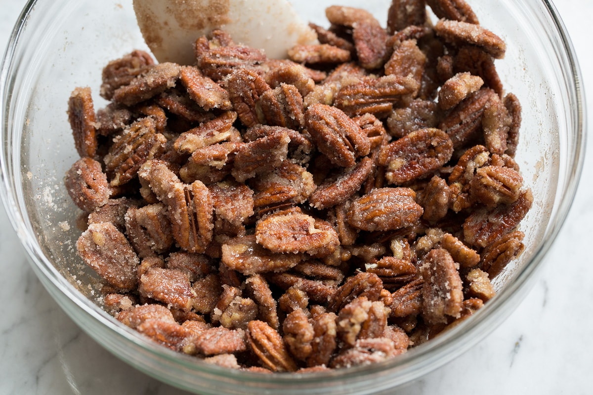 Nuts coated in sugar mixture in mixing bowl.