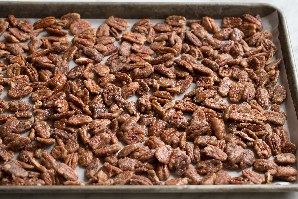 Pecans coated with sugar spread out on a baking sheet. 