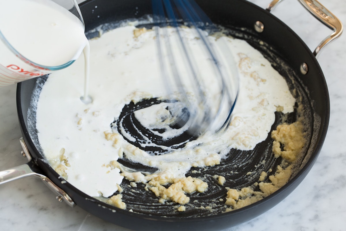 Whisking milk to roux in skillet.