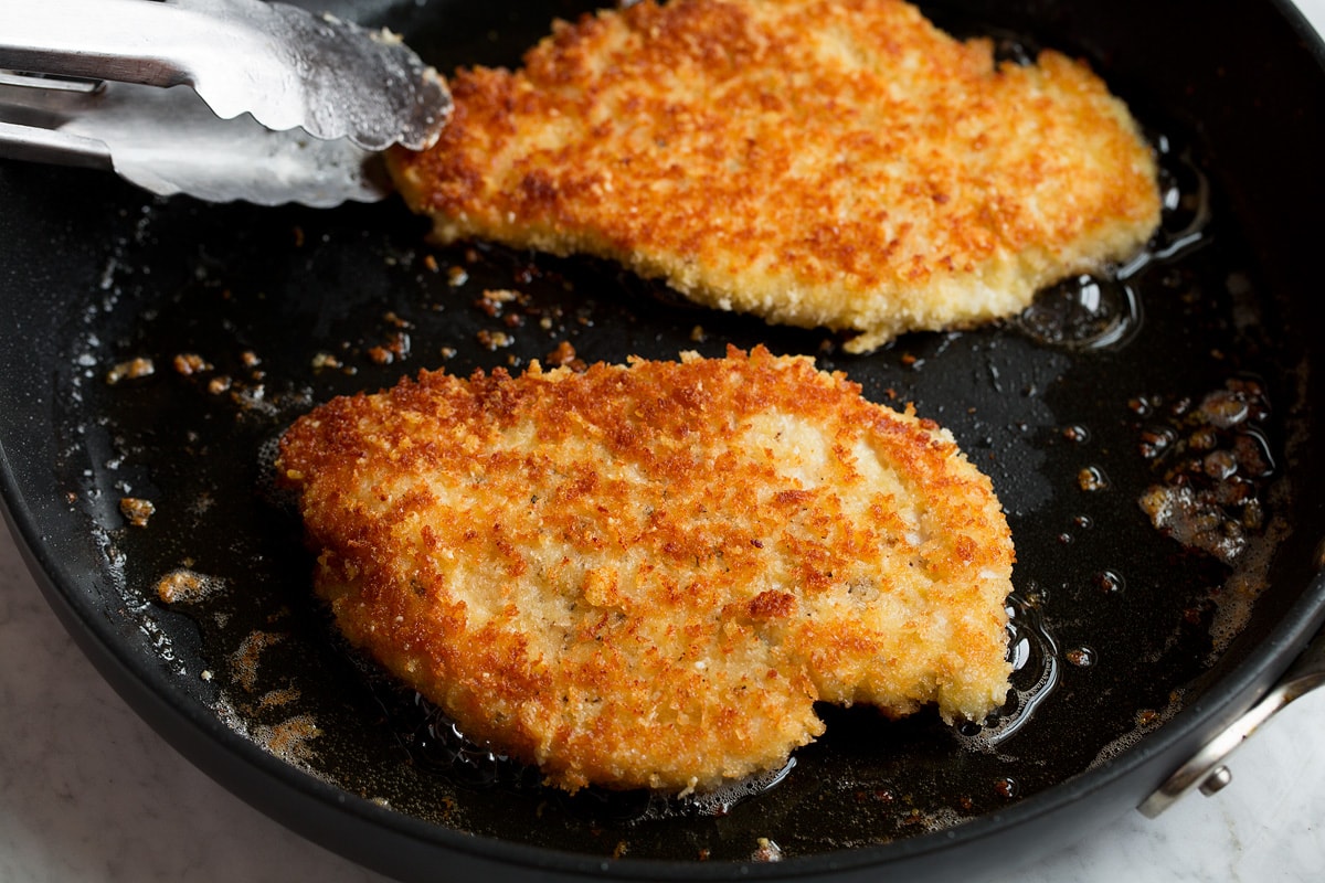 Parmesan chicken shown being fried in a skillet.