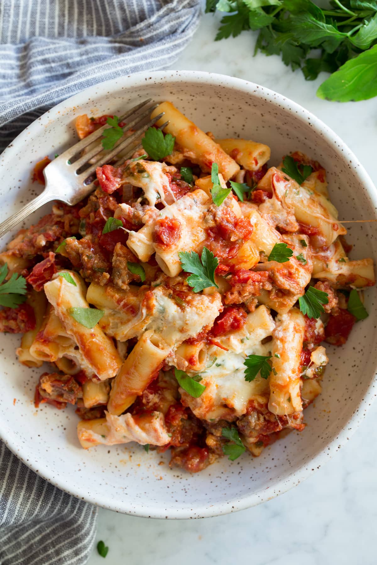 Bowl of baked ziti including ziti pasta, sausage, marinara sauce, three types of Italian cheese and fresh herbs.