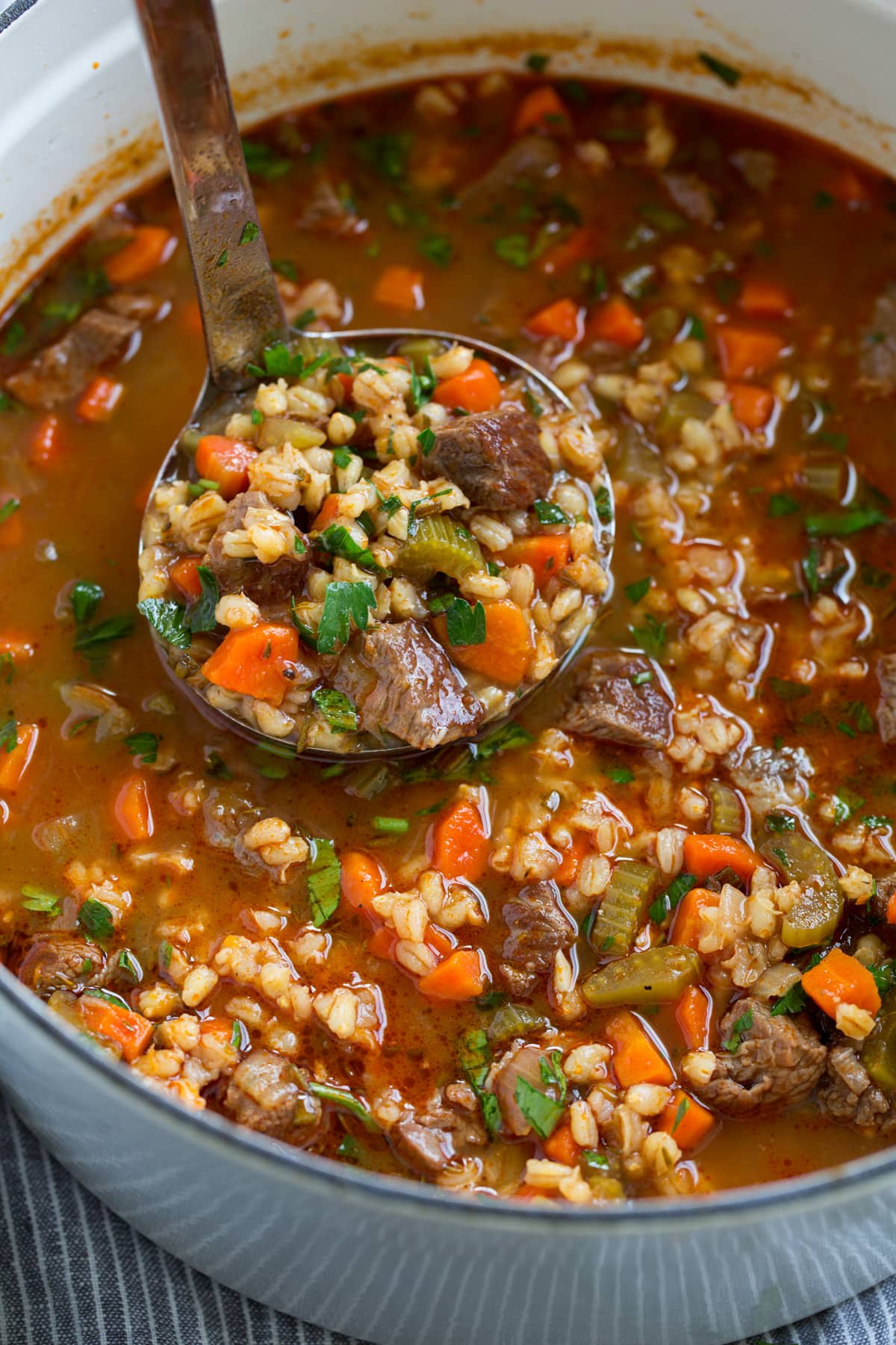 Ladle full of beef and barley soup shown close up.