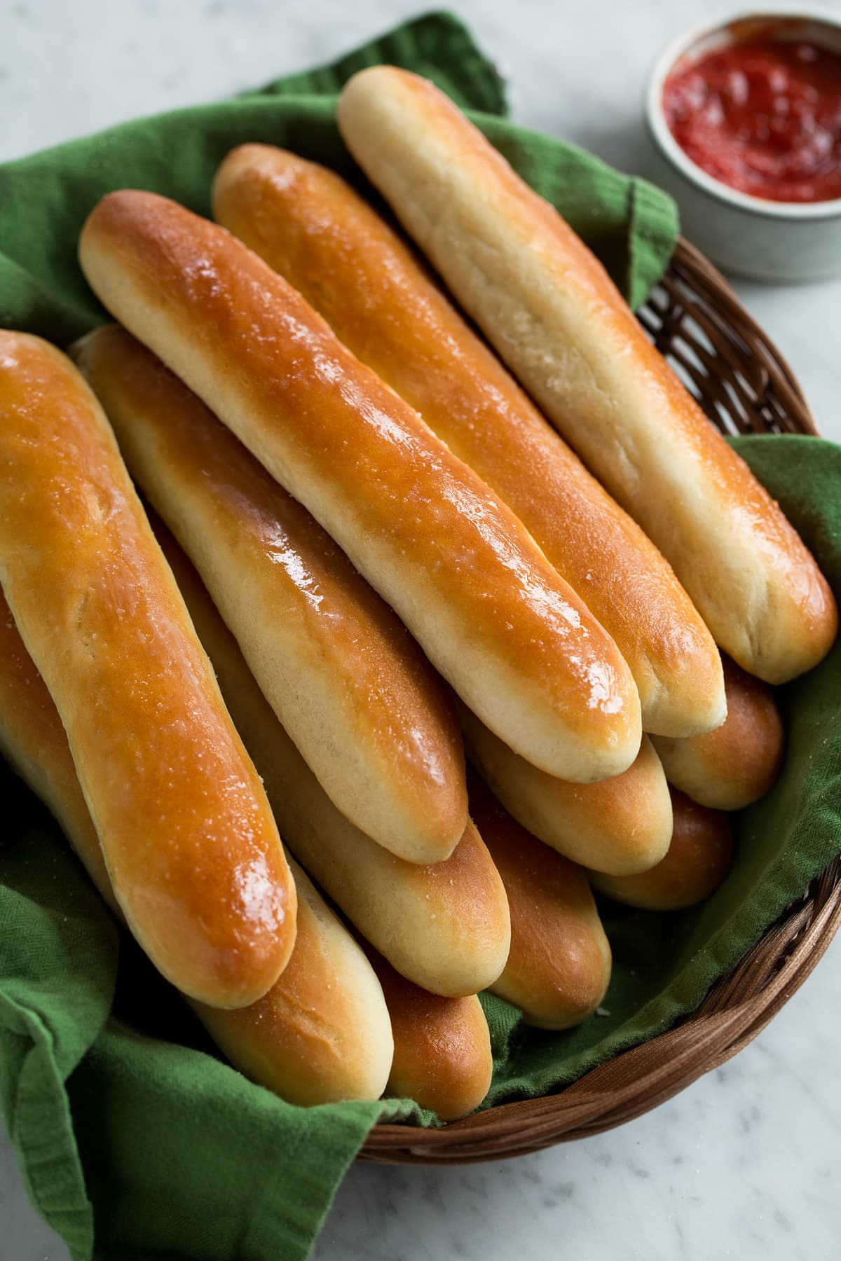 Breadsticks stacked in a wicker basket lined with a green kitchen cloth.