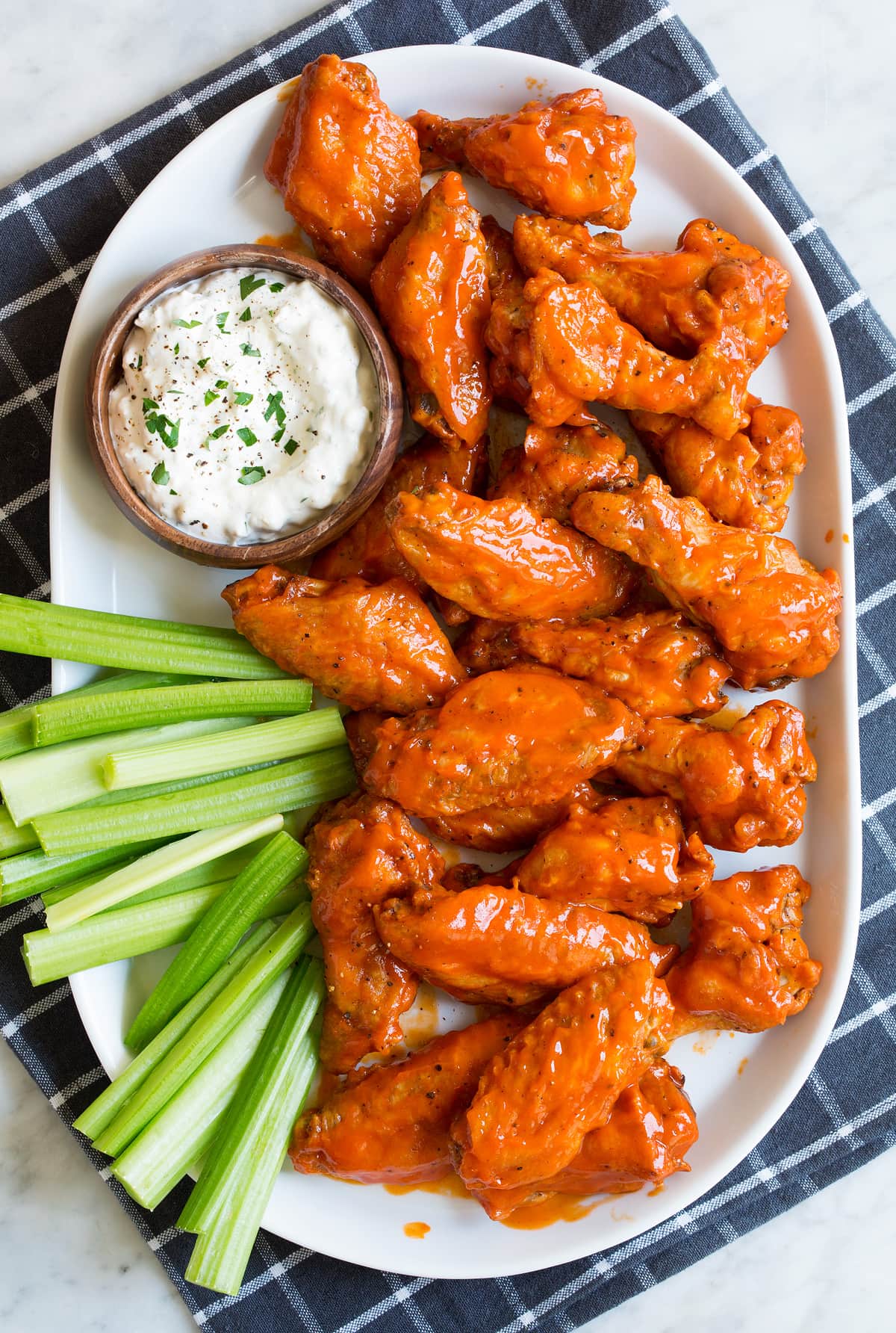 Baked Buffalo Wings Platter full of buffalo wings coated in a buffalo wing sauce served with a side of blue cheese sauce and celery sticks.