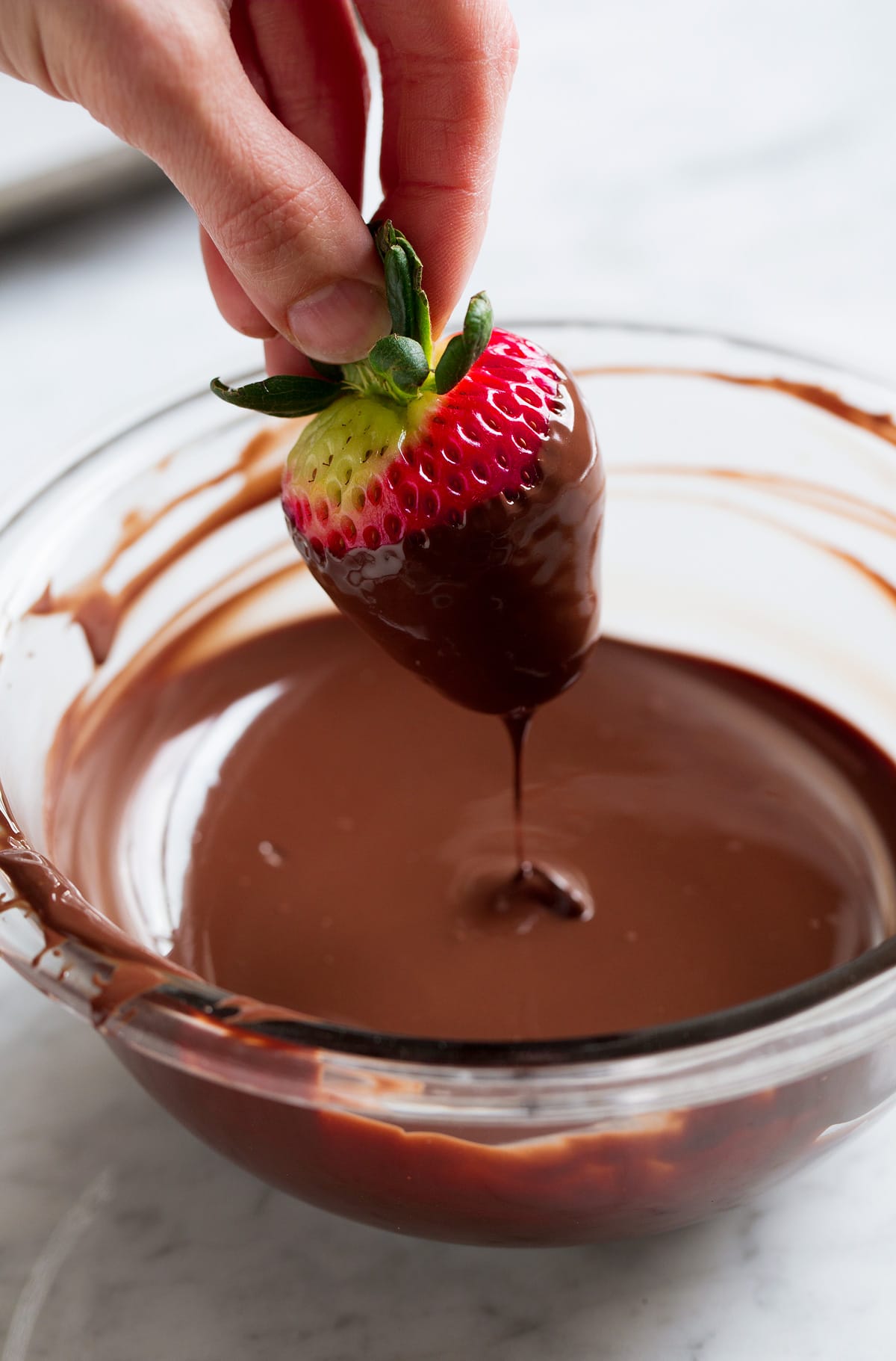 Chocolate Covered Strawberries Hand holding strawberry by leaves and dipping strawberry in melted chocolate.