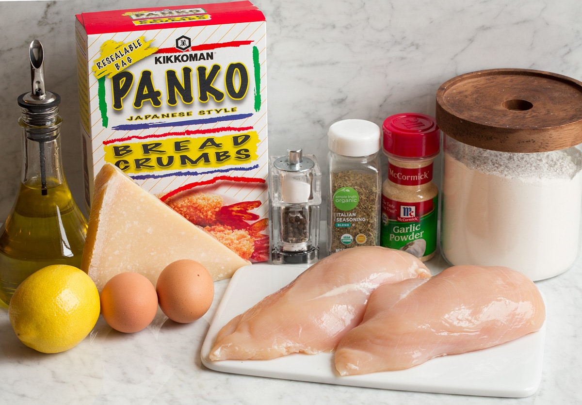 Photo of ingredients in parmesan crusted chicken. Includes chicken breasts, panko bread crumbs, flour, eggs, garlic powder, Italian seasoning, lemon, parmesan, olive oil, salt and pepper.