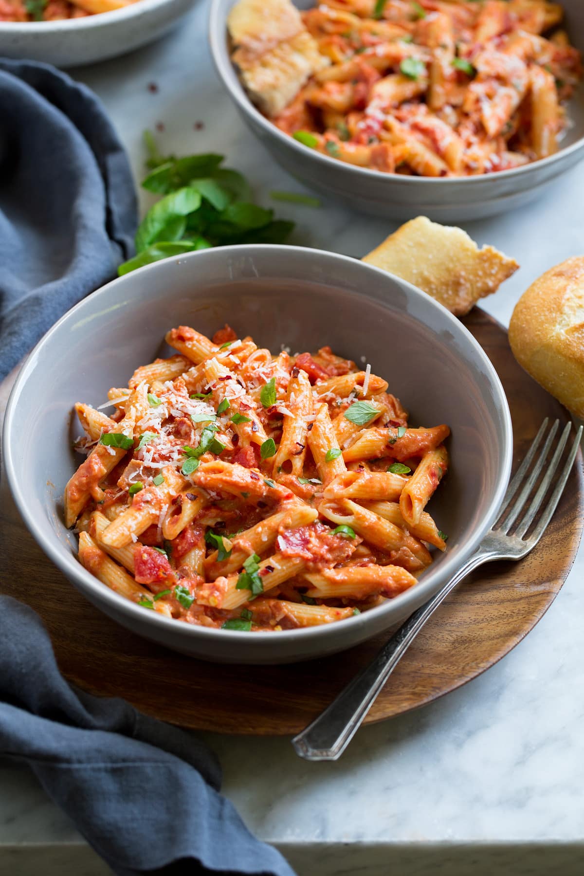 Two servings of penne alla vodka in grey serving bowls set over wooden plates.