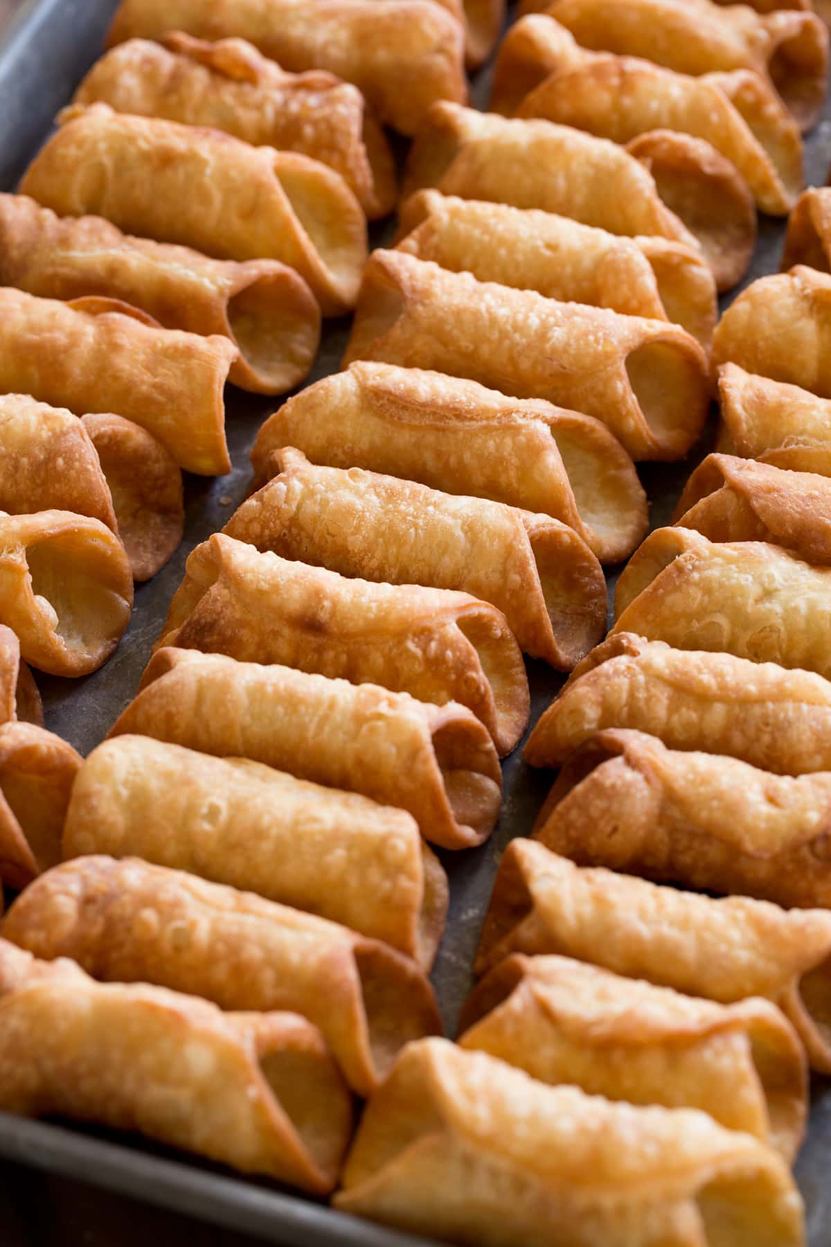 Homemade fried cannoli shells on a baking sheet shown before filling.