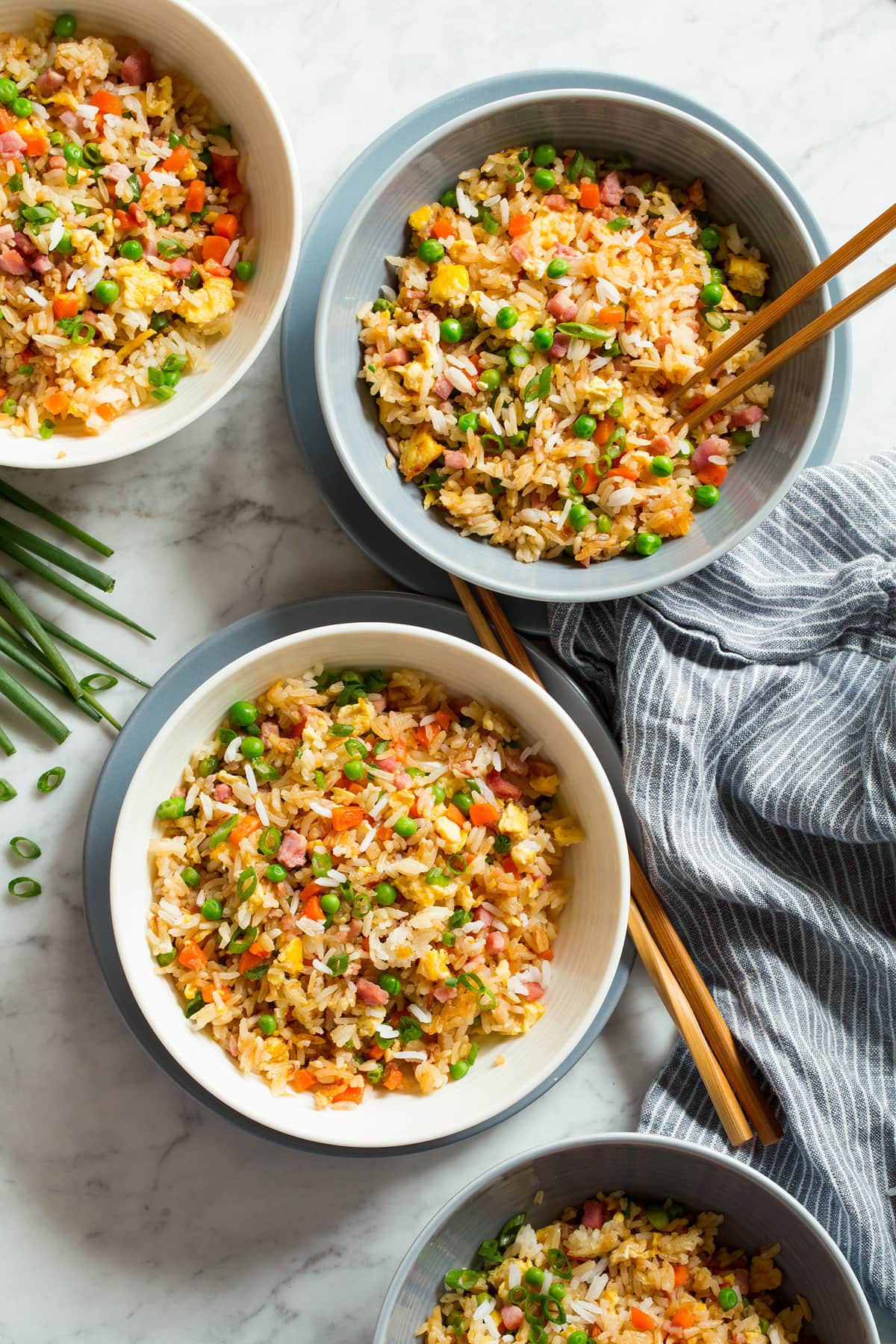 Fried Rice Four servings of fried rice shown overhead in white serving bowls set over blue plates with chopsticks to the side.