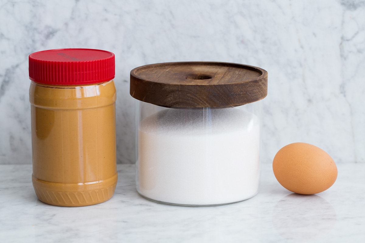 Image of ingredients including creamy peanut butter, granulated sugar in a glass jar and 1 egg.