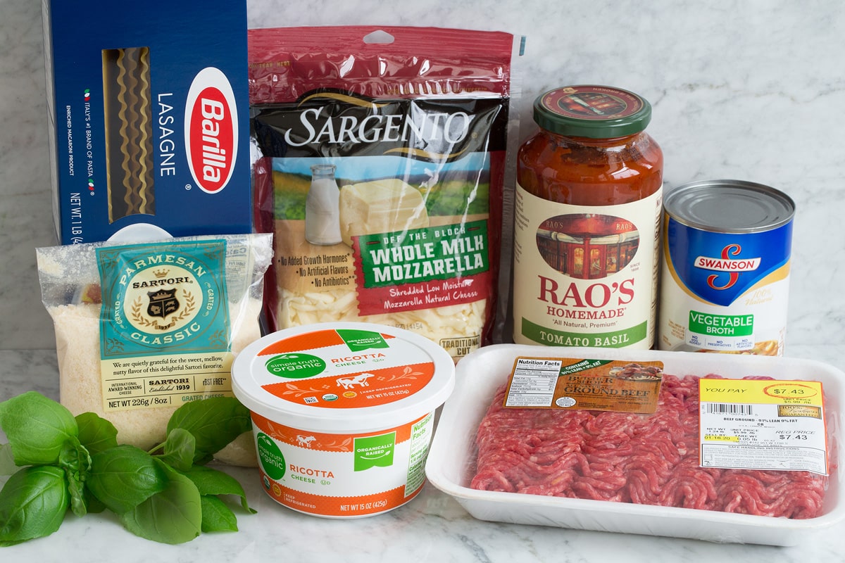 Image showing ingredients used to make an easy lasagna. Includes lasagna noodles, parmesan, basil, ricotta, mozzarella, bottled marinara, ground beef and vegetable broth.