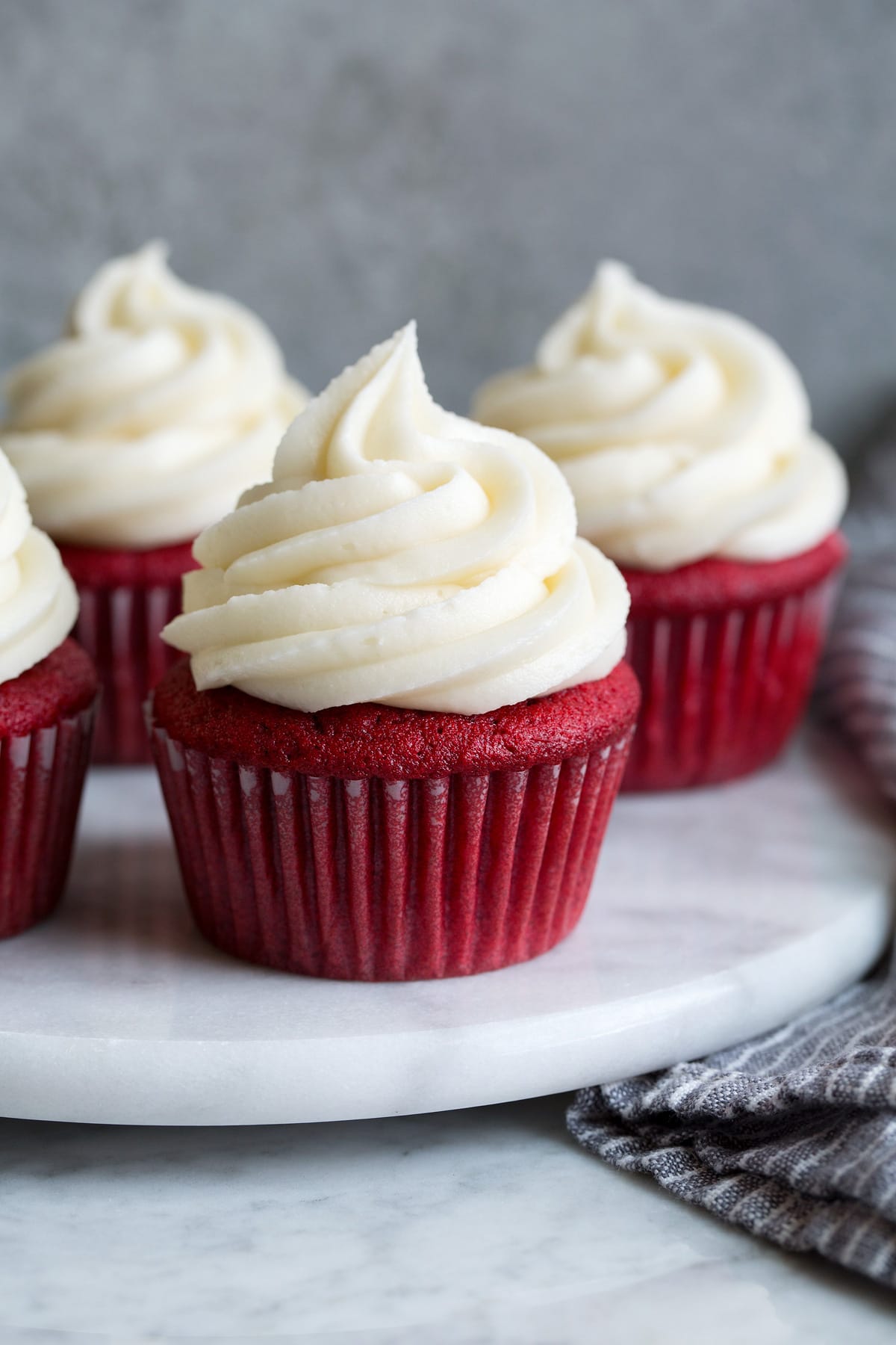 Cream cheese frosting shown atop four red velvet cupcakes on a marble platter.