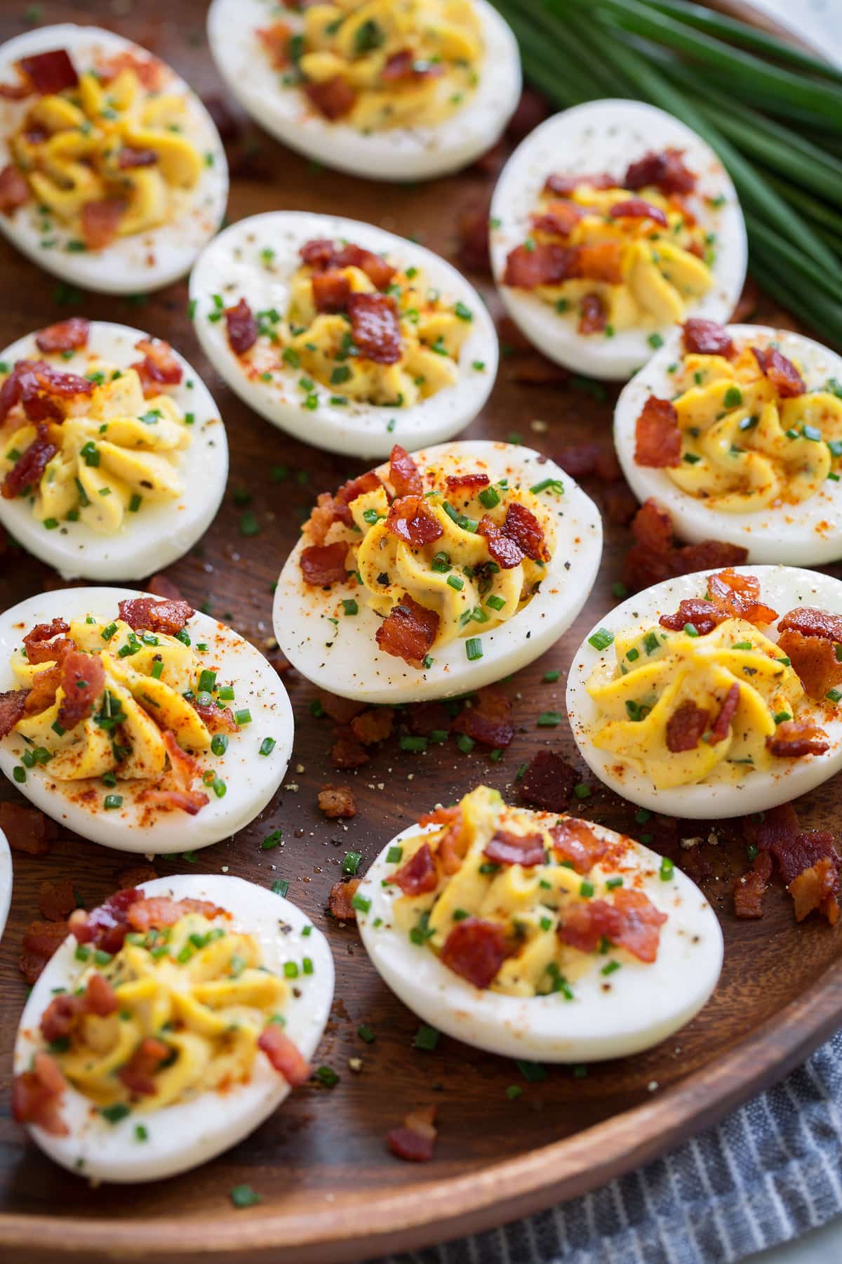 Wooden plate filled with deviled eggs. Eggs filled with a creamy mayonnaise and egg yolk filling and are garnished with chives and bacon.