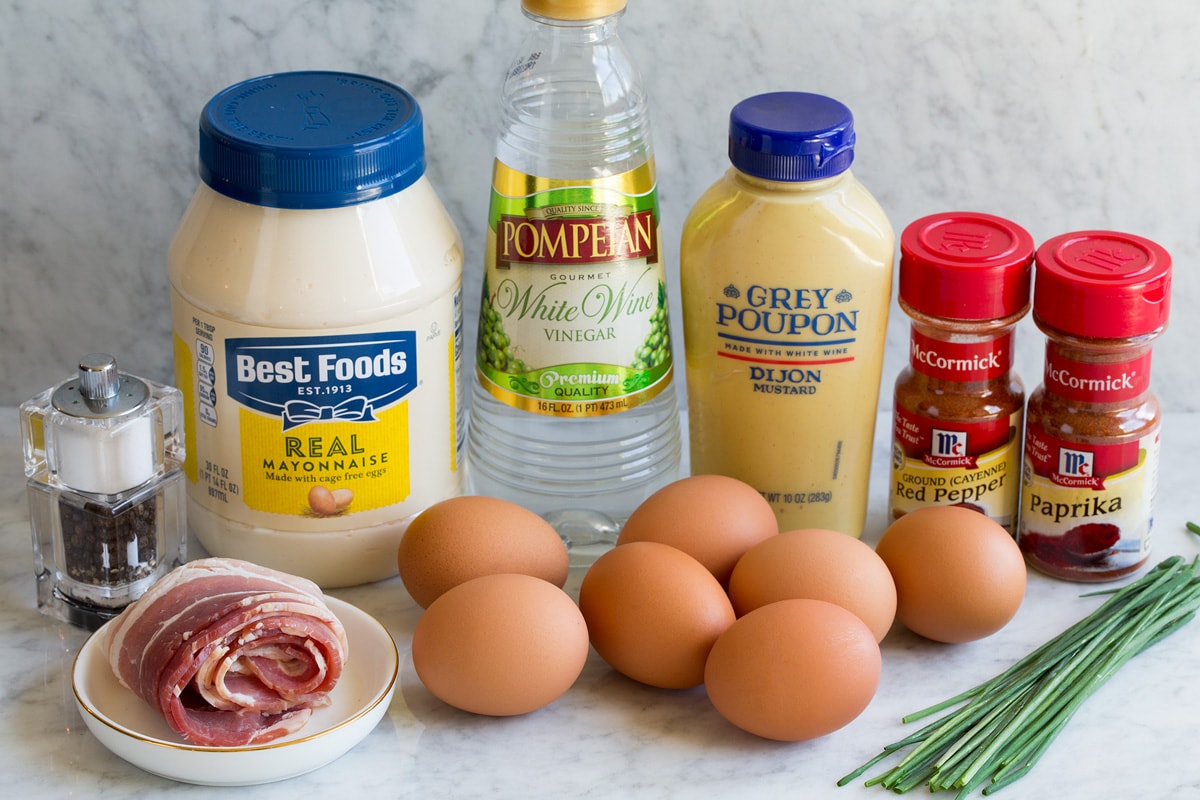 Image showing ingredients that go into deviled eggs including mayonnaise, dijon mustard, white wine vinegar, eggs, chives, cayenne pepper, paprika, chives and bacon.