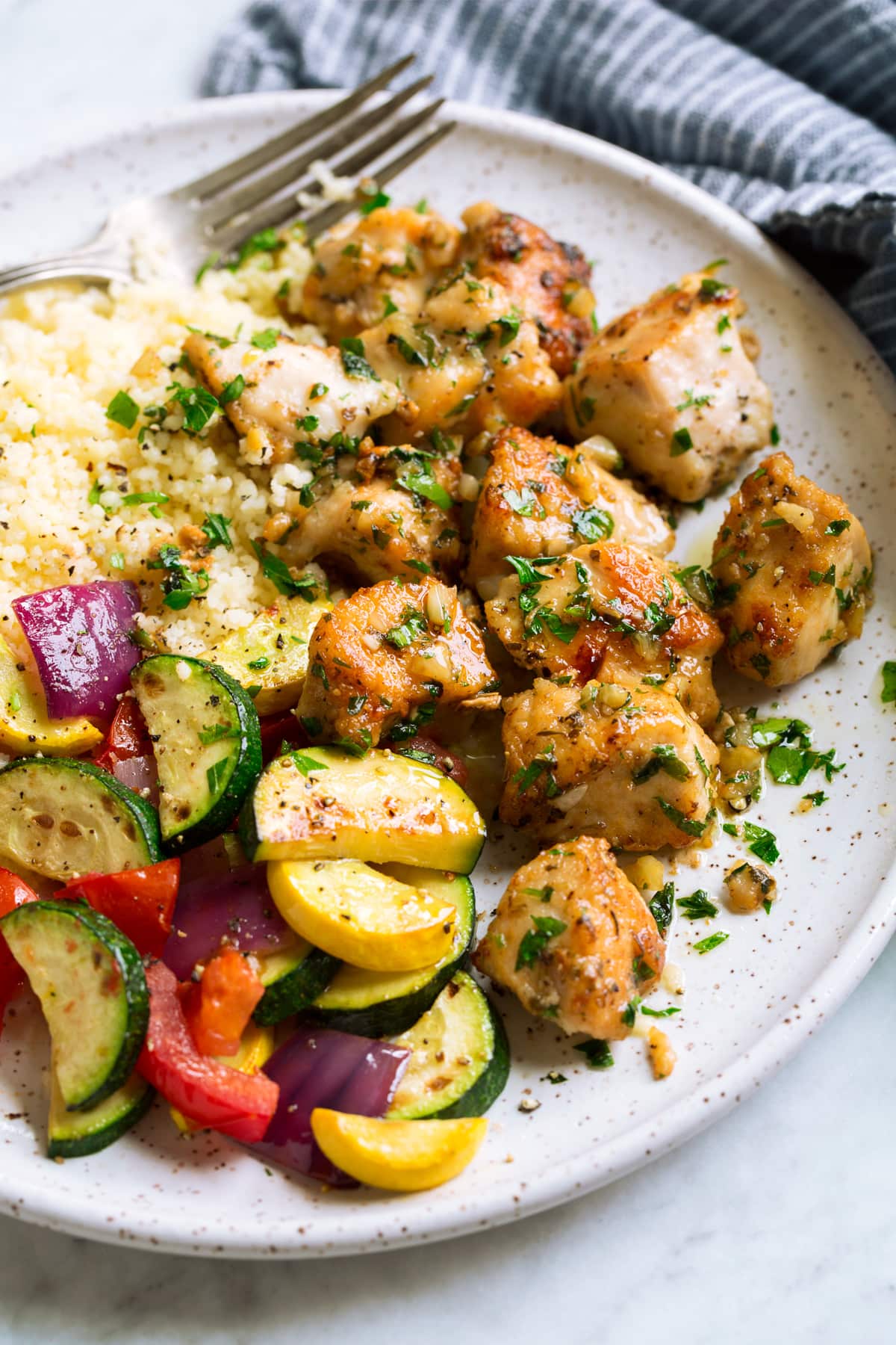 Chicken bites on a white serving plate with a side of couscous and vegetables.