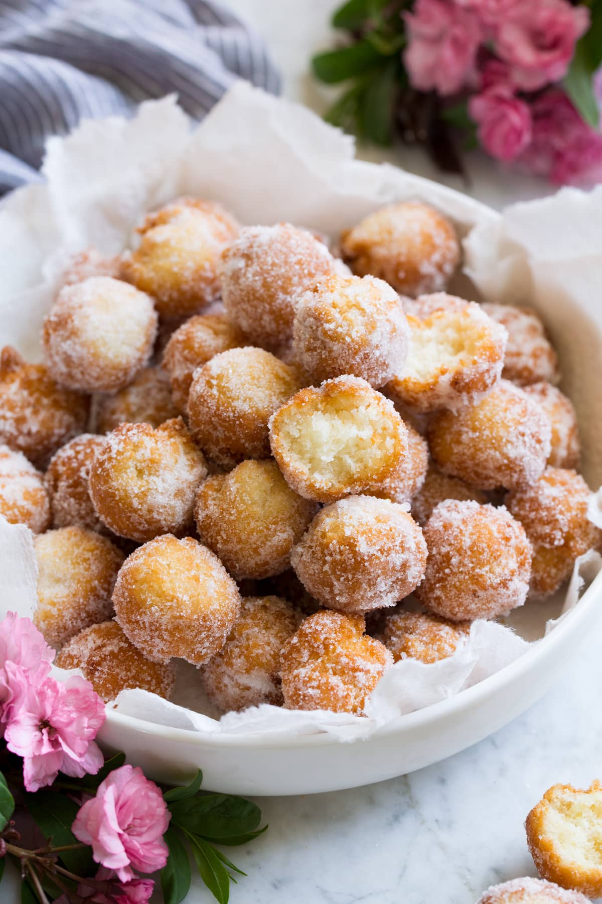 Homemade donuts in a serving bowl. Two are bitten into to show texture of interior.