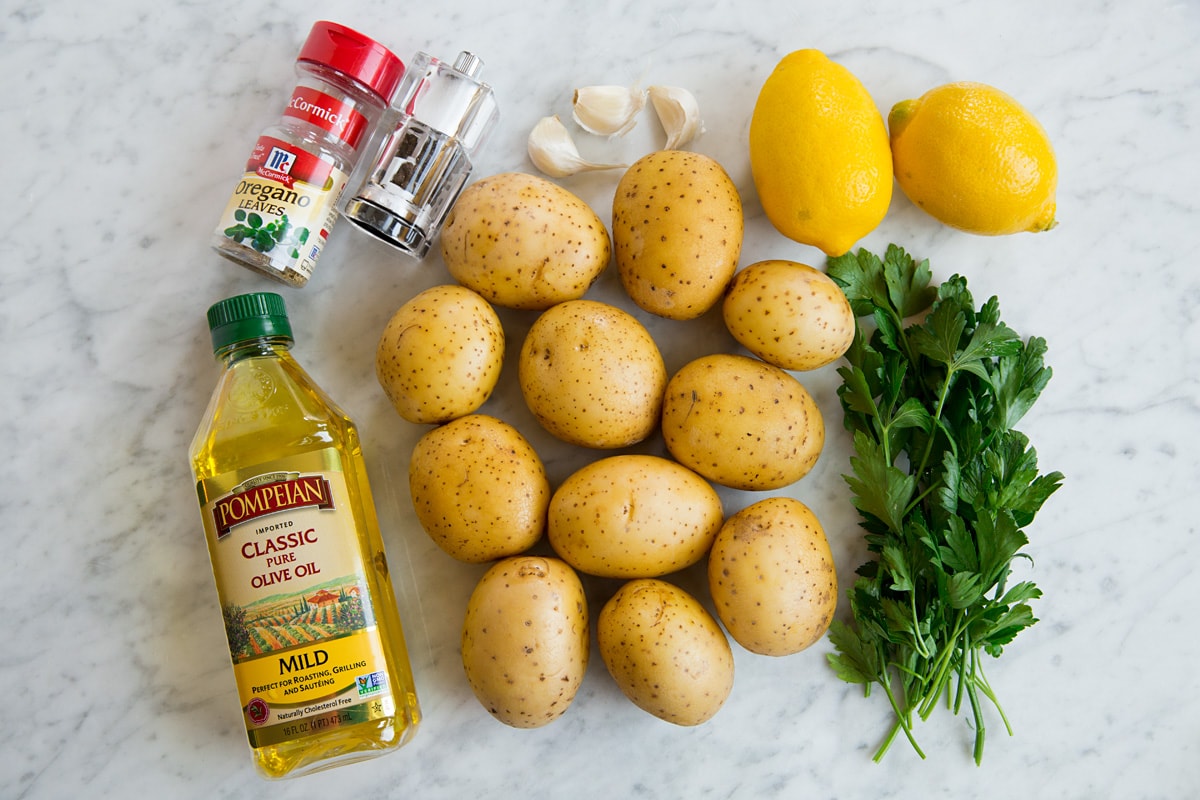 Image of ingredients used to make lemon potatoes including yukon gold potatoes, lemons, olive oil, garlic, oregano, salt, pepper and parsley.