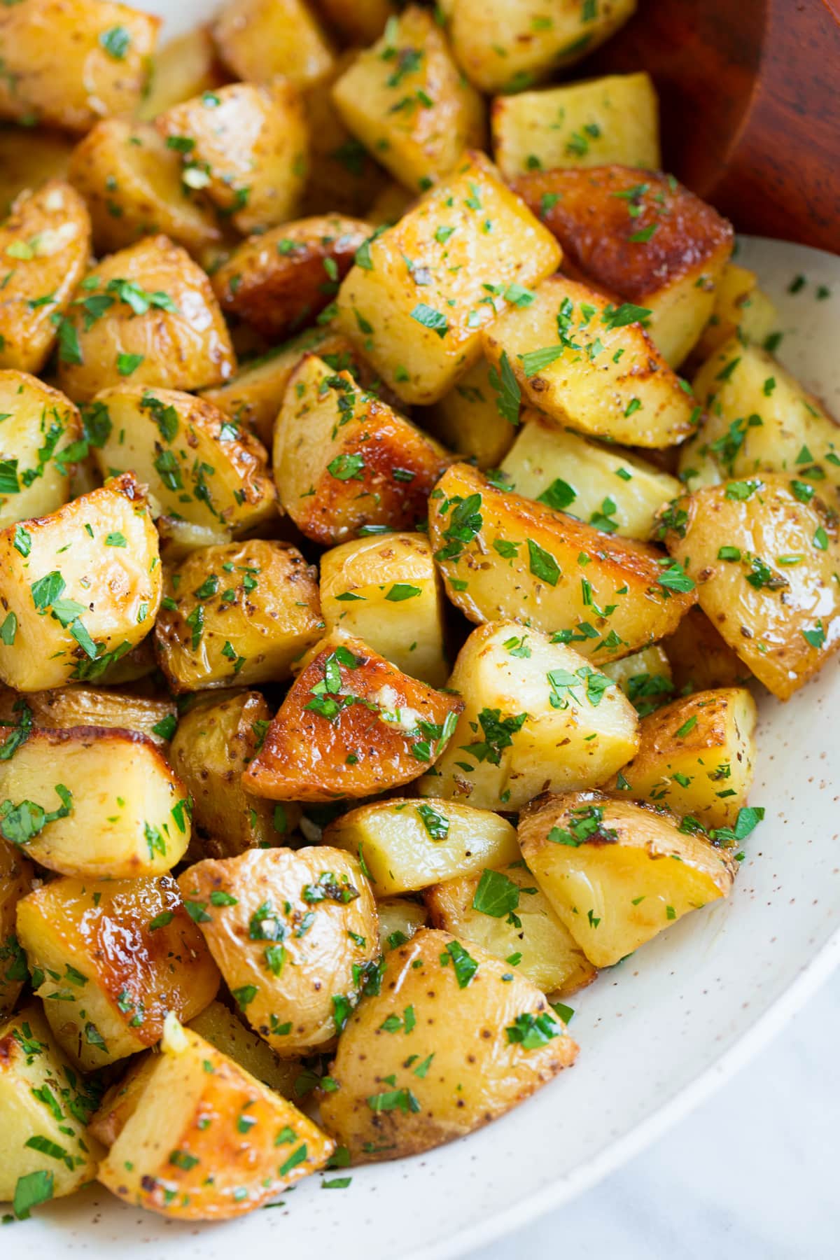 Close up image of roasted potatoes with lemon and parsley in a white serving bowl.