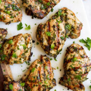 Close up image of grilled chicken with herbs on a white platter.