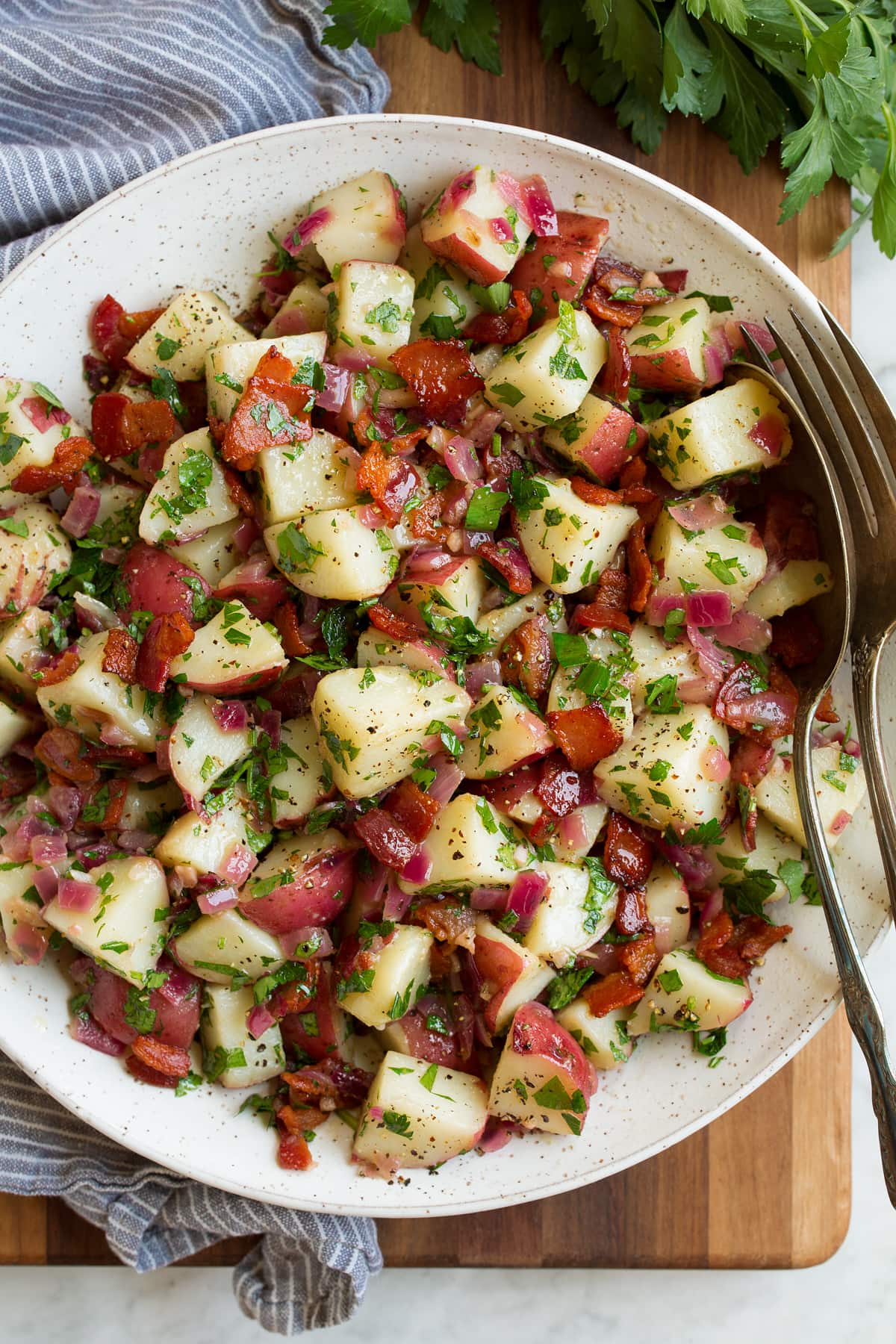Overhead image of german potato salad in a bowl with a grey striped napkin to the side.