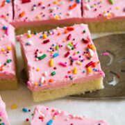 Close up image of sugar cookie bar decorated with pink frosting and sprinkles. It is being scooped up with a serving spatula.