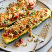 Two stuffed zucchini boats on a white dinner plate with a fork to the side.