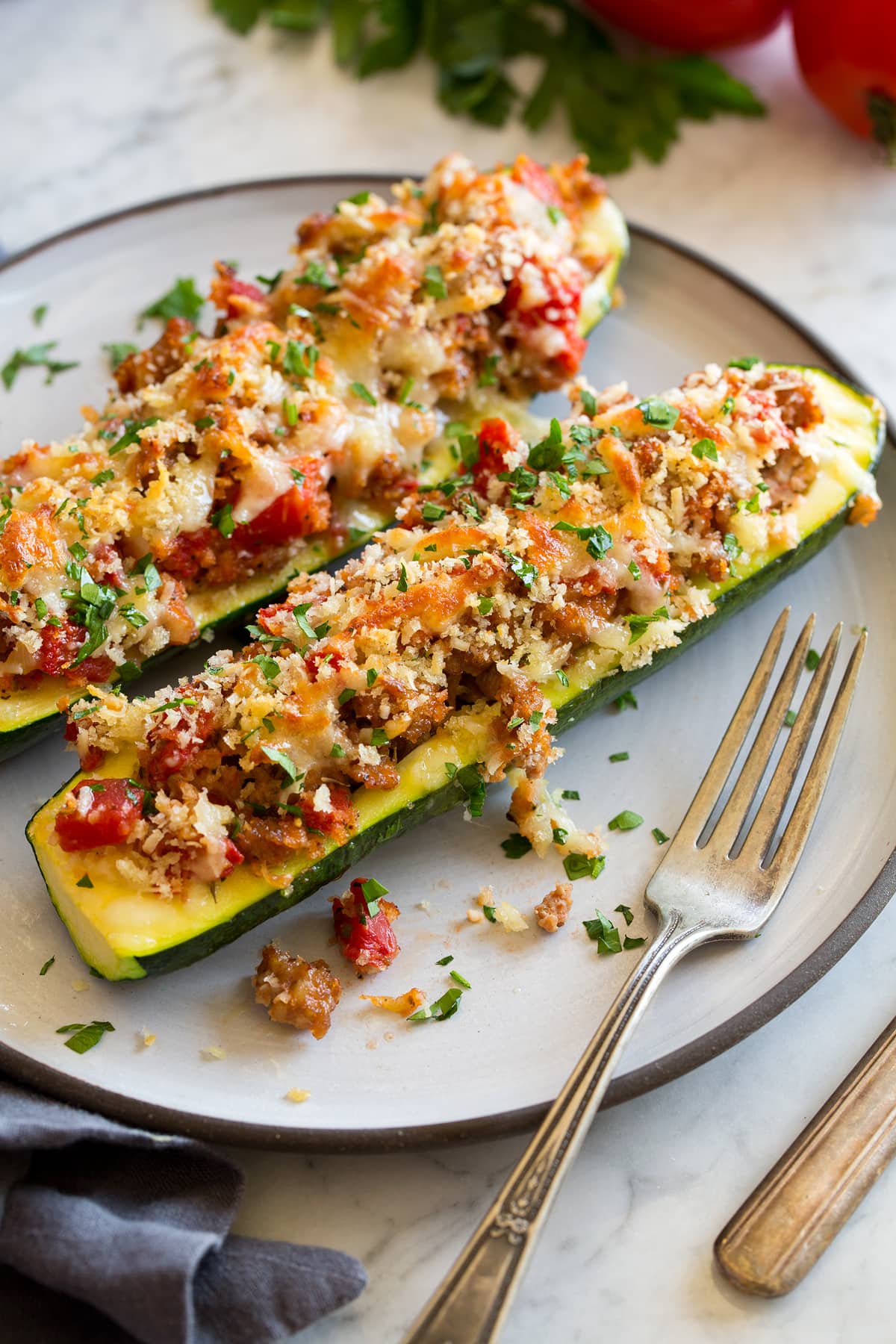 Two stuffed zucchini boats on a white dinner plate with a fork to the side. 