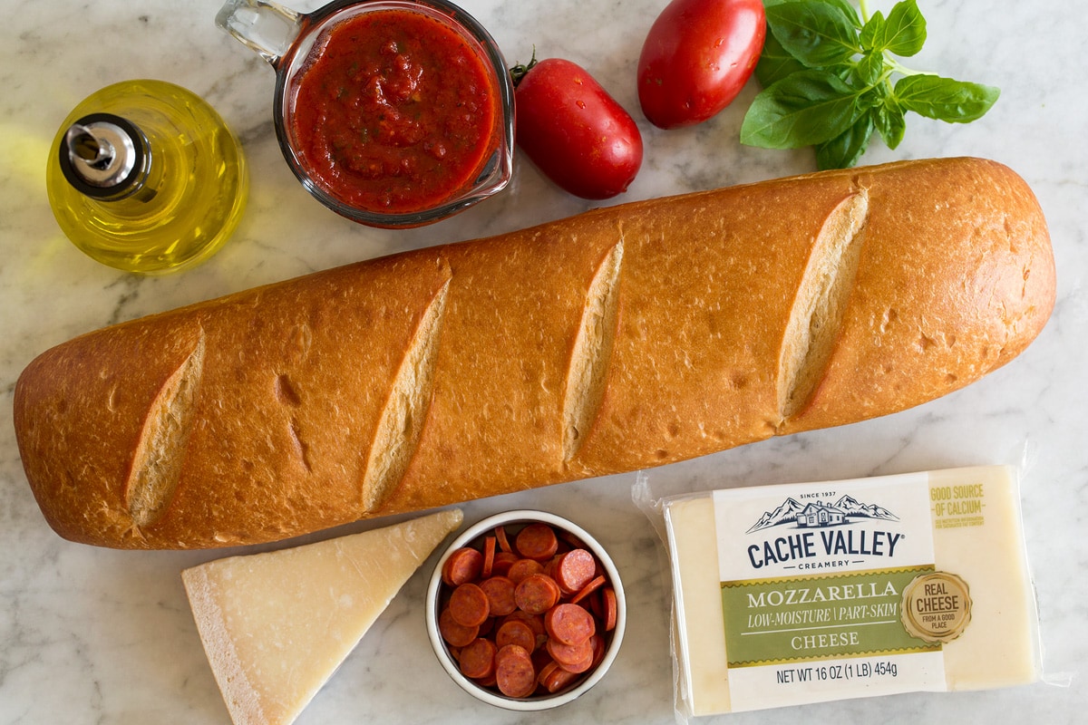 Image showing ingredients used to make French bread pizza. Includes French bread, cheeses, basil, pizza sauce, olive oil, pepperoni, tomatoes and basil.