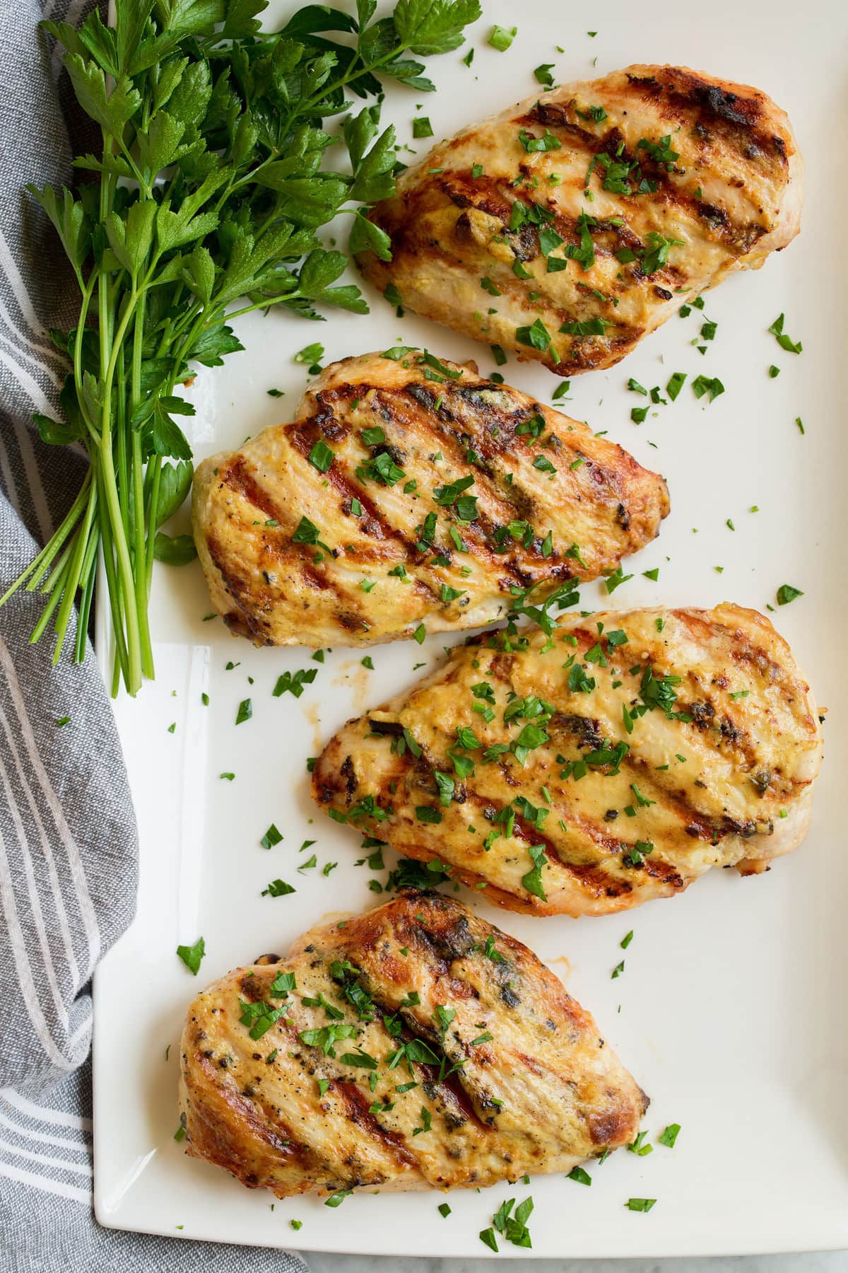 Overhead image of four chicken breasts that have been coated with a dijon mustard sauce and grilled. Chicken is resting on a rectangular white platter with a side of parsley.