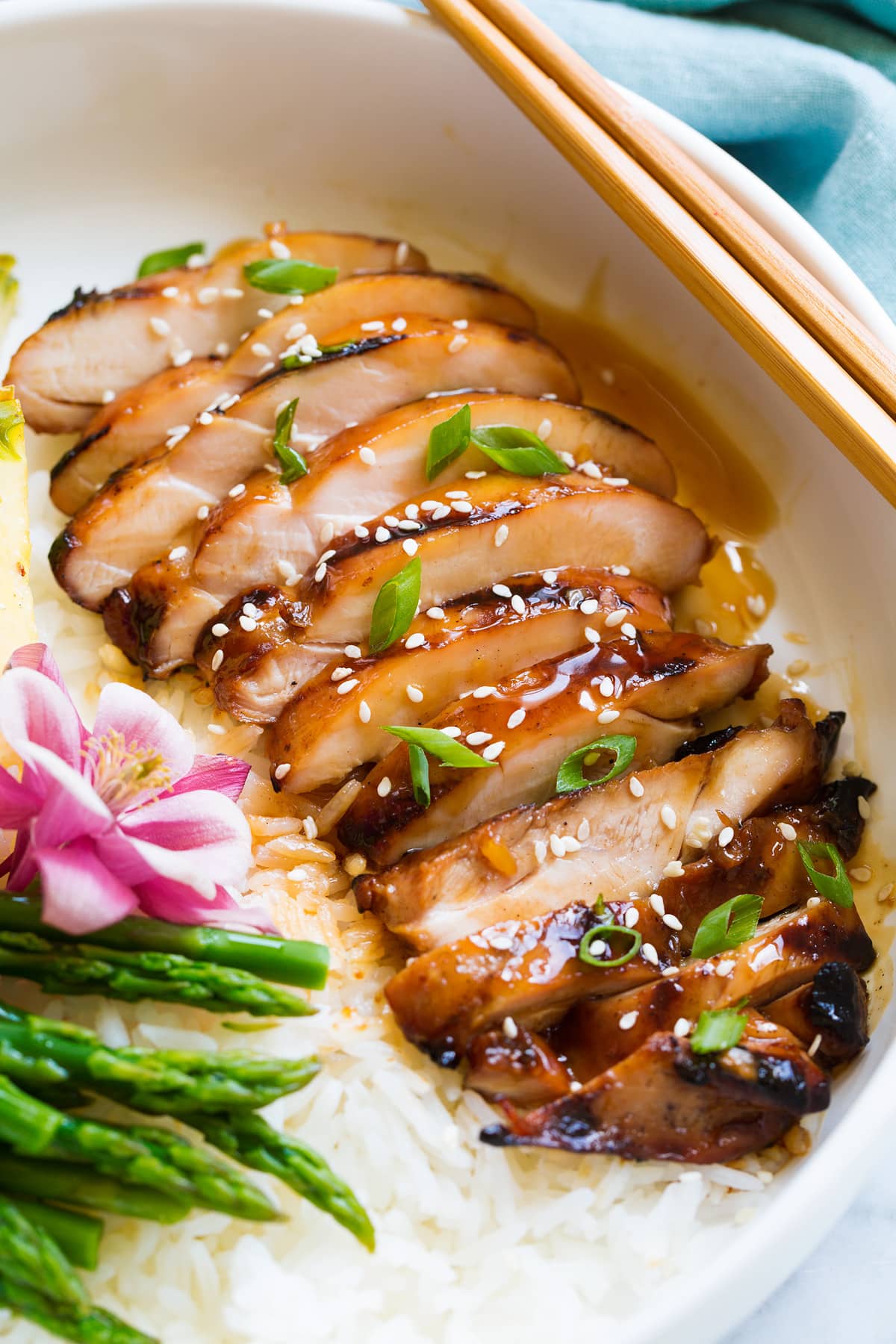 Sliced chicken thigh shown after cooking, covered in teriyaki sauce, sesame seeds and green onions.