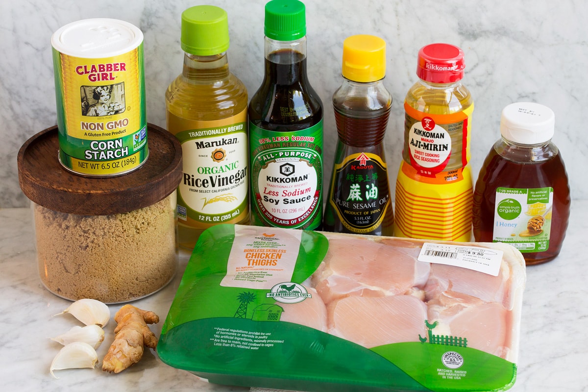 Image of ingredients used to make teriyaki chicken marinade. Includes soy sauce, rice vinegar, mirin, sesame oil, brown sugar, honey, ginger, garlic, chicken thighs and cornstarch.