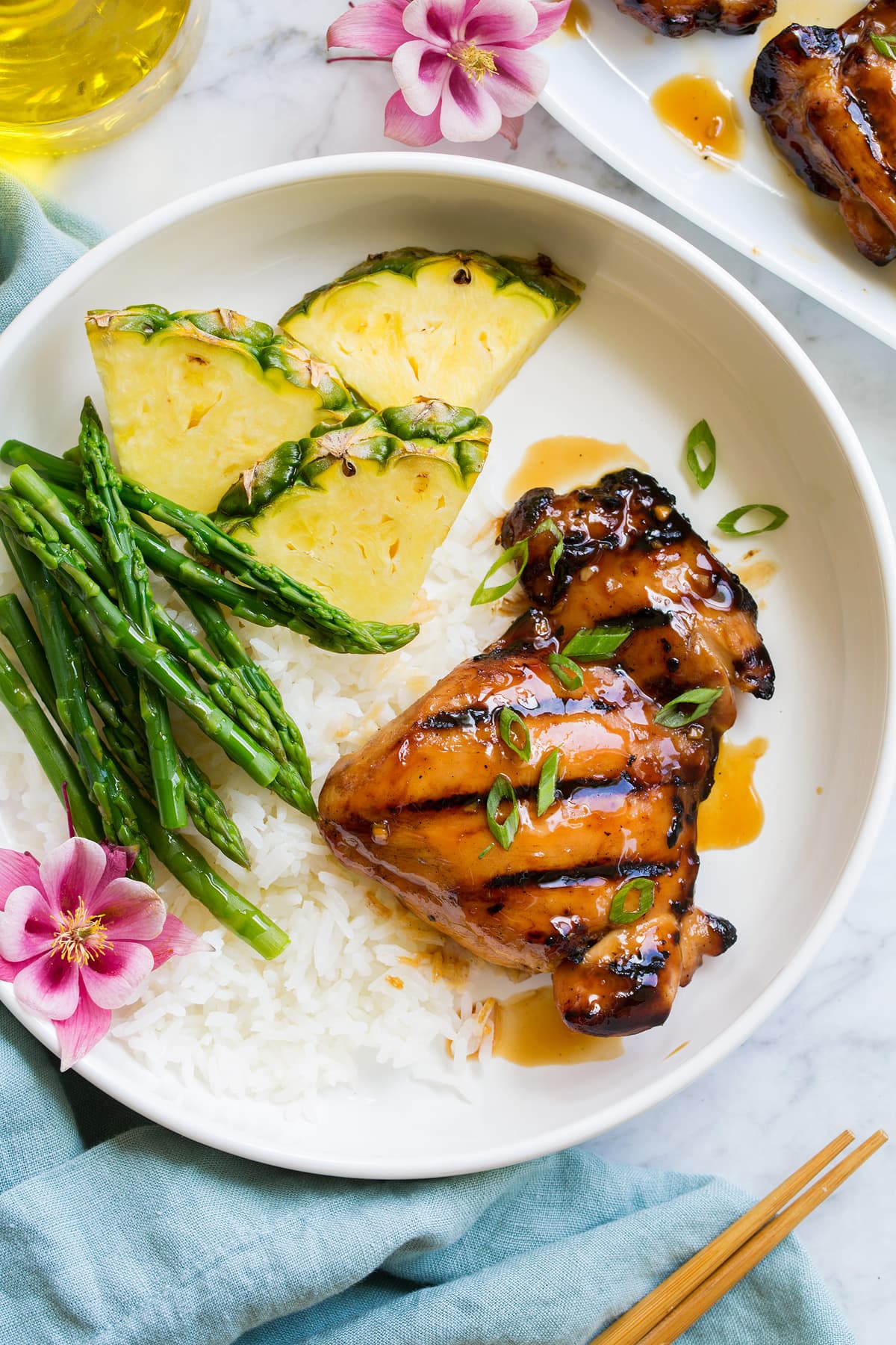 Piece of marinated and grilled teriyaki chicken shown served with rice, asparagus and fresh pineapple.