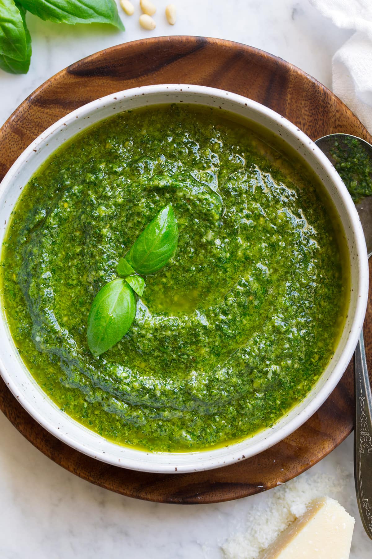 Basil Pesto Image shown overhead of pesto in a white bowl resting on a wooden platter.