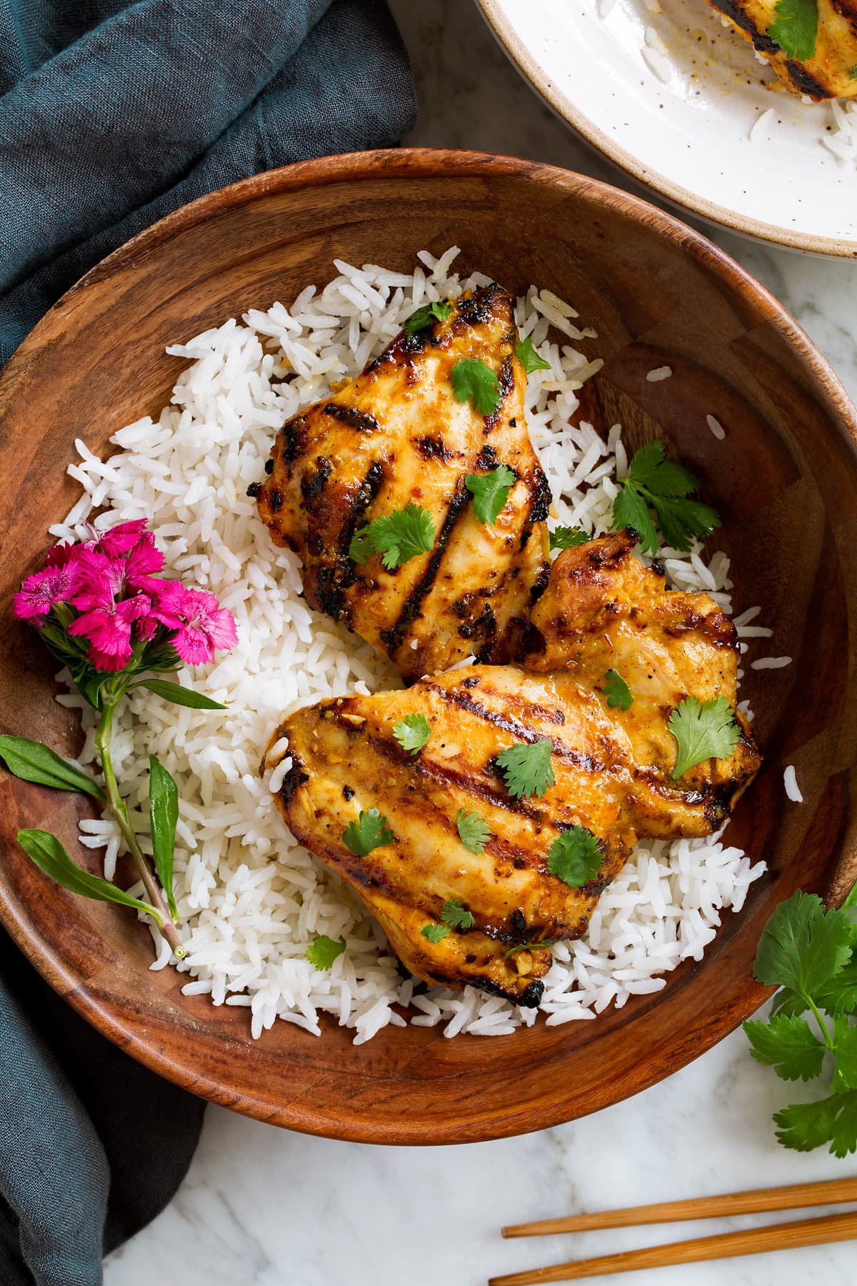 Thai Coconut Grilled Chicken Thighs in a wooden serving bowl with rice and decorative flowers.